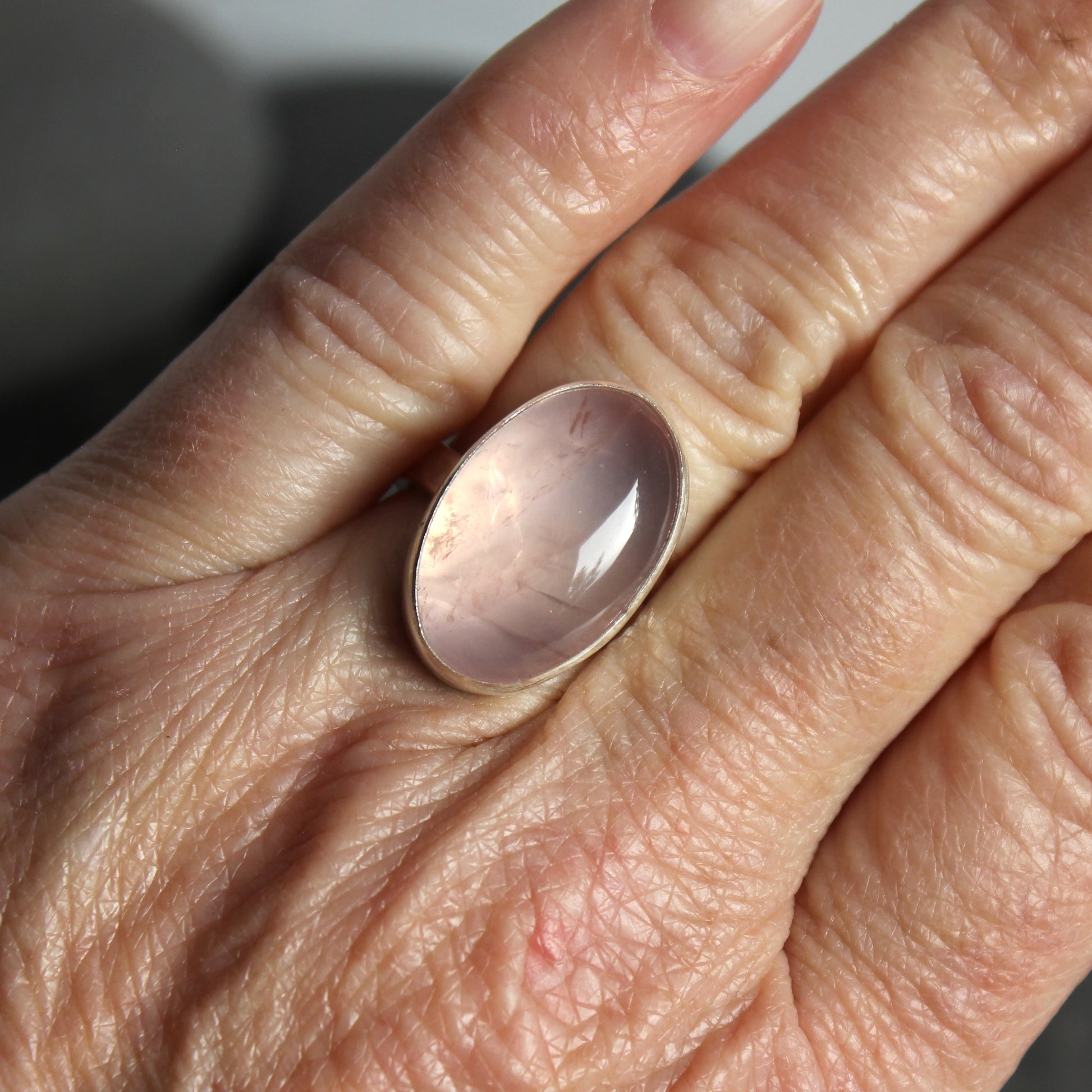 Close-up of a hand wearing a ring with a pink rose quartz stone.