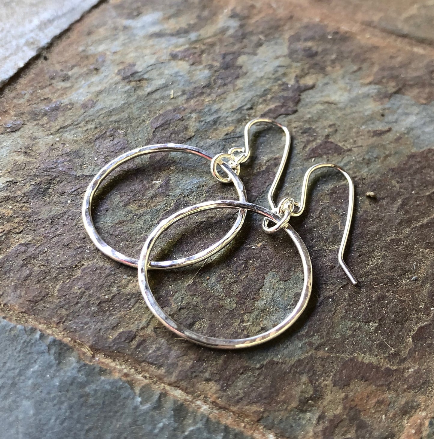 Silver hoop earrings on a stone surface