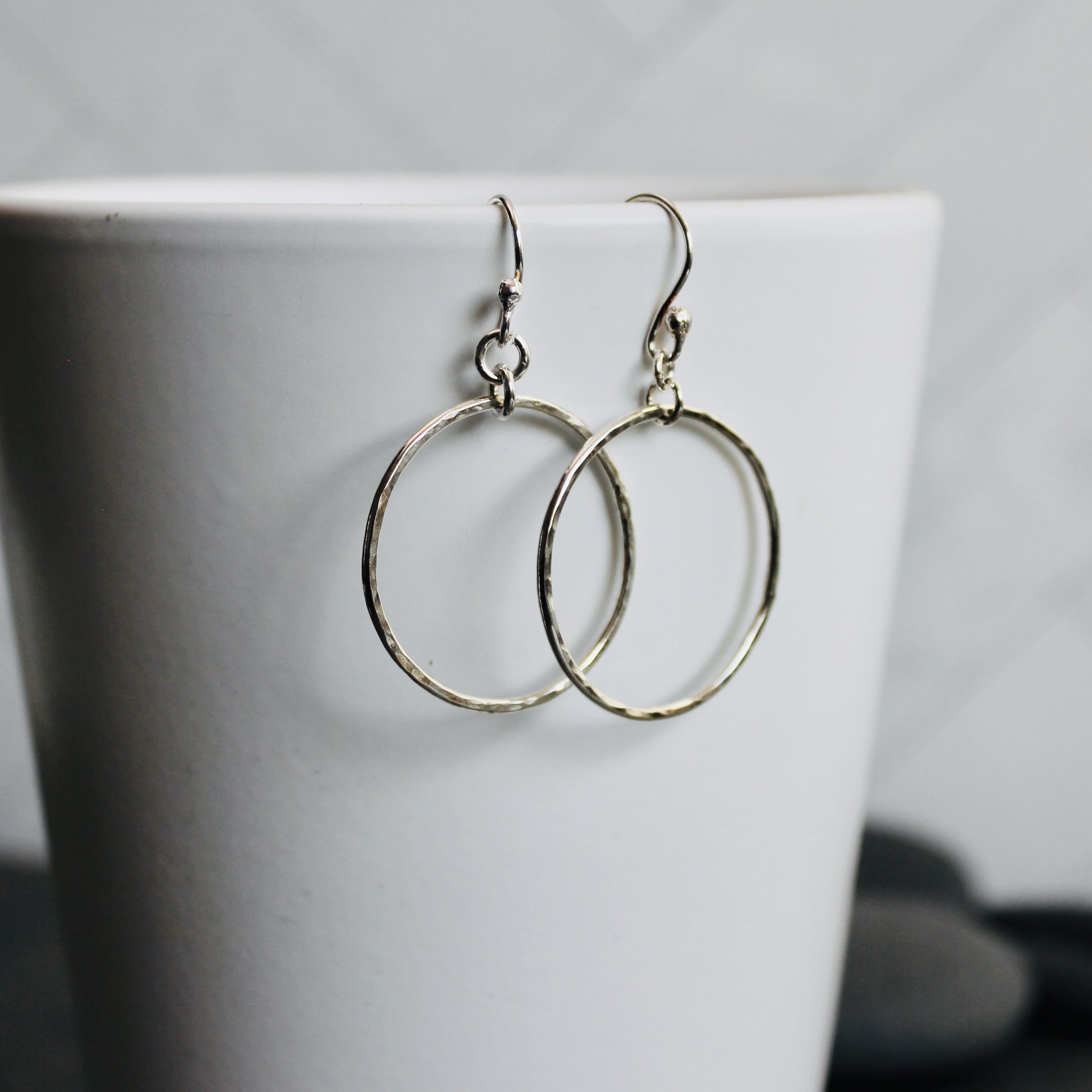 Silver hoop earrings on a white surface with a blurred background