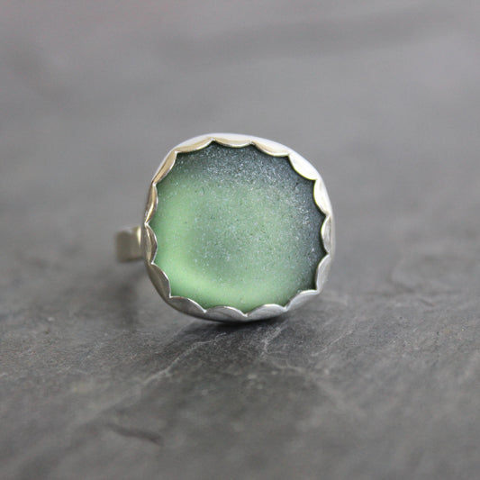 Green sea glass ring with silver band on a gray background