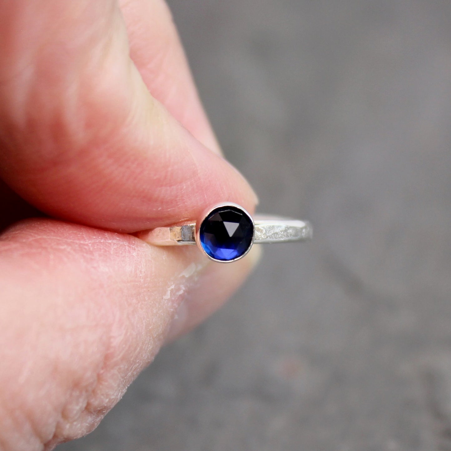 Silver ring with a blue gemstone held between fingers against a blurred background