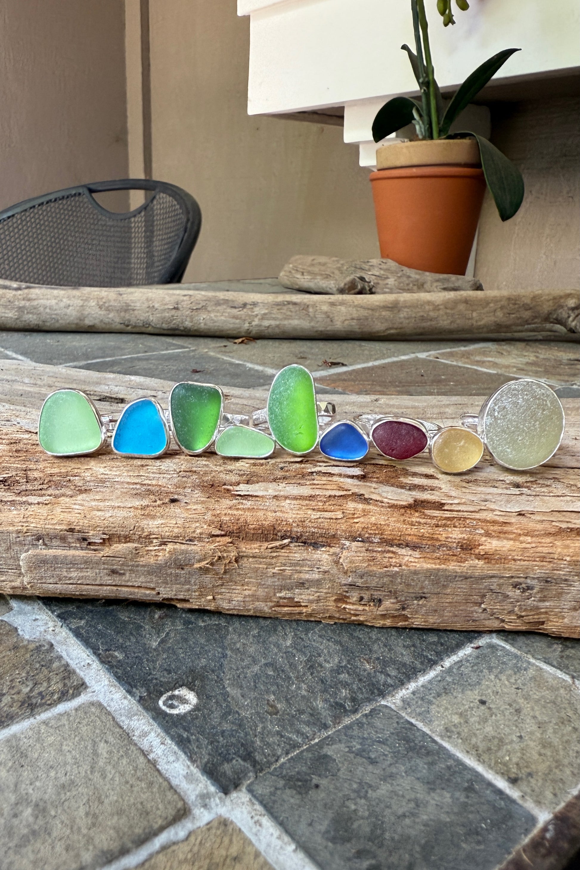 Colorful sea glass rings on a wooden surface with a plant in the background.