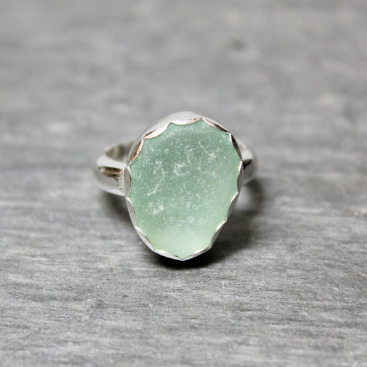 Green sea glass ring with silver band on a gray background