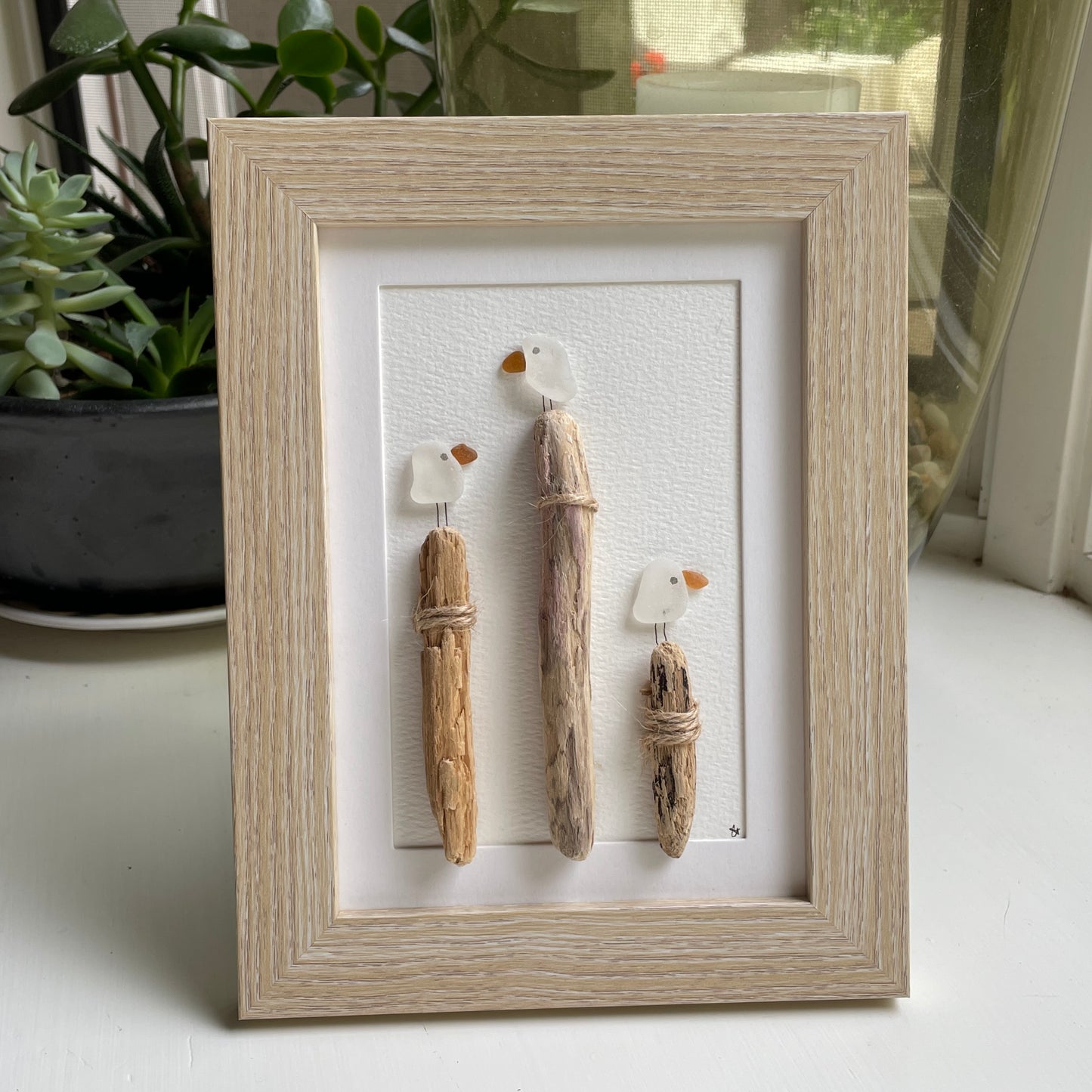 This is a framed 5 x 7 inch sea glass art picture featuring seagulls and driftwood logs. This item is perfect for gift giving and is ready to hang or place on a shelf. 