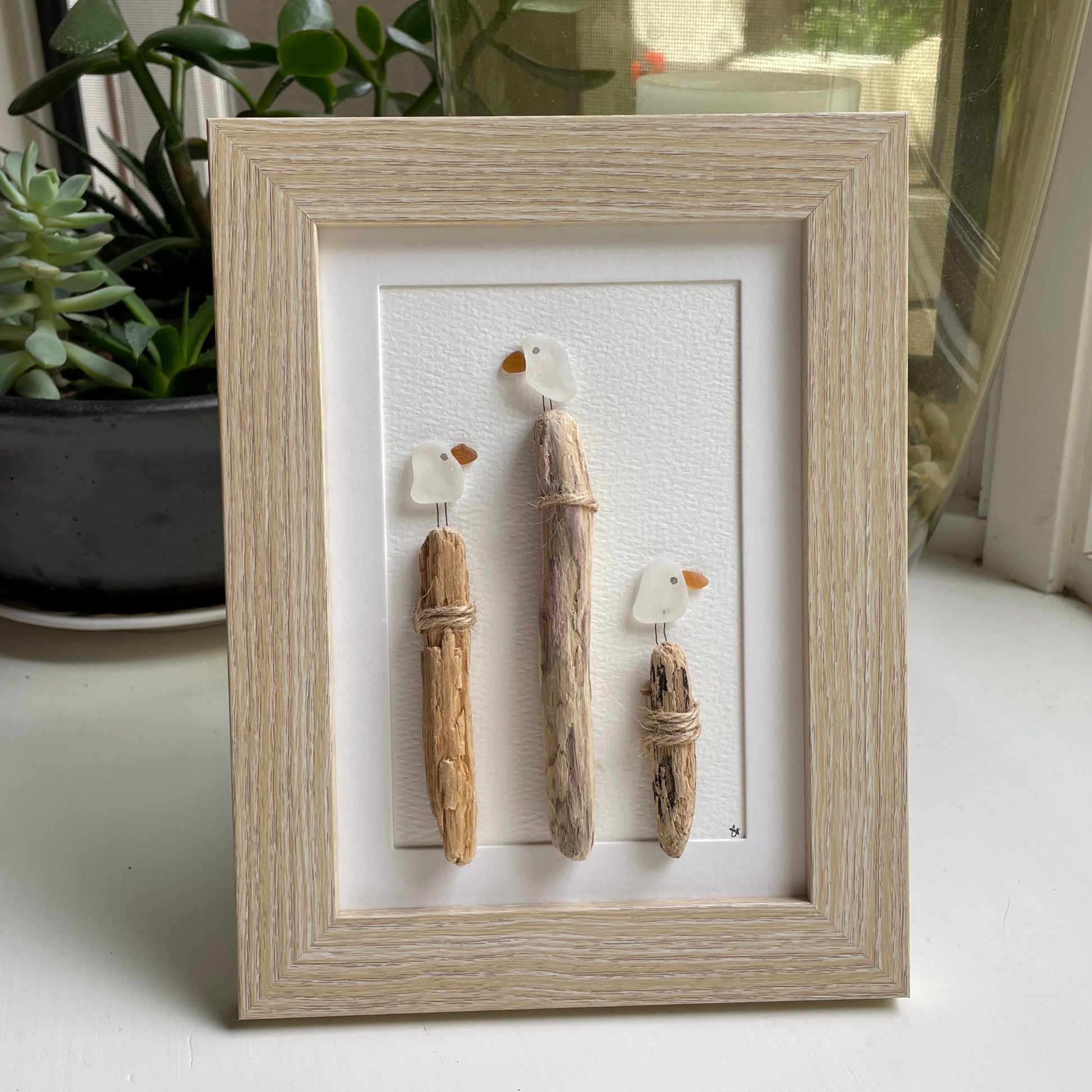 This is a framed 5 x 7 inch sea glass art picture featuring seagulls and driftwood logs. This item is perfect for gift giving and is ready to hang or place on a shelf. 