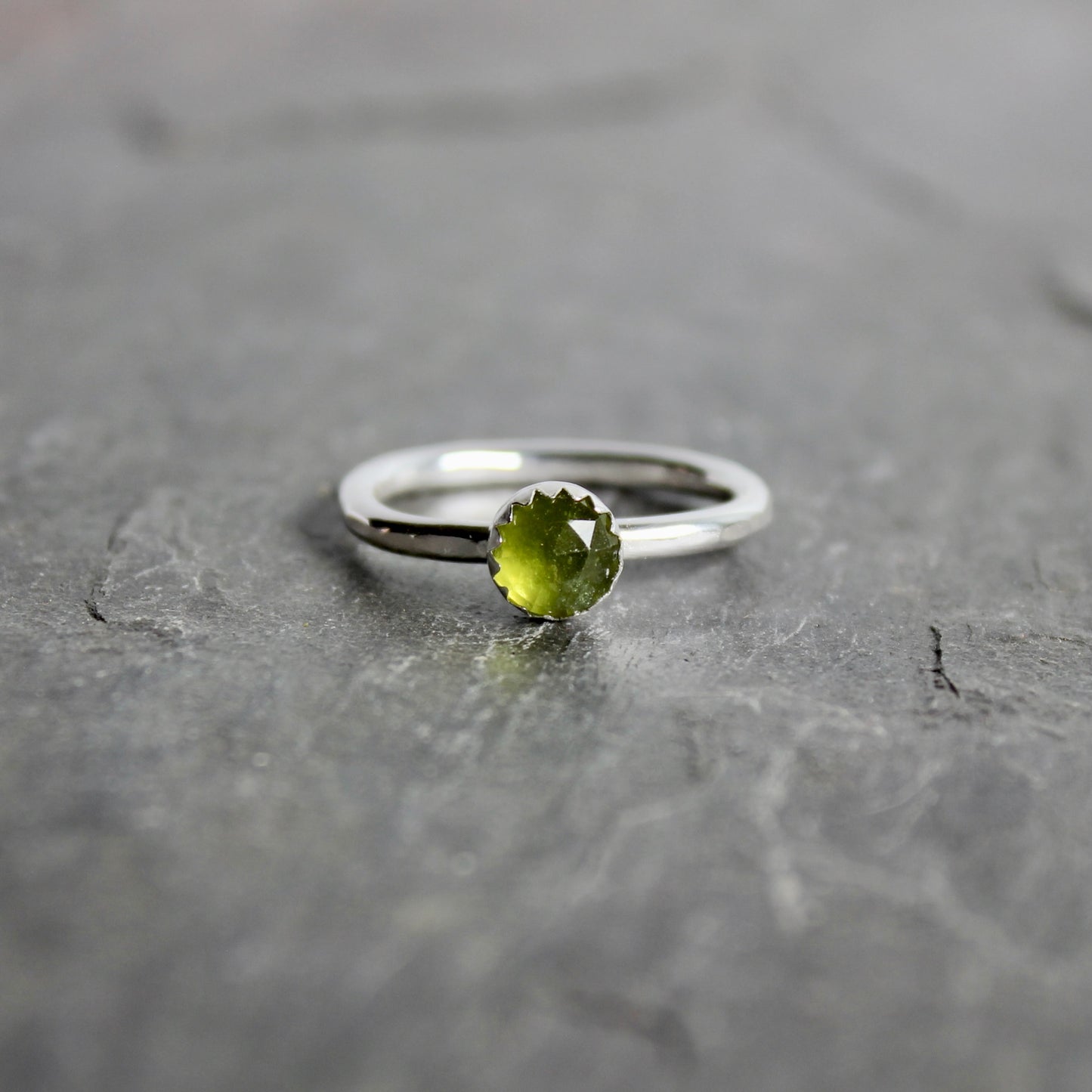 Silver ring with a green serpentine gemstone on a gray surface
