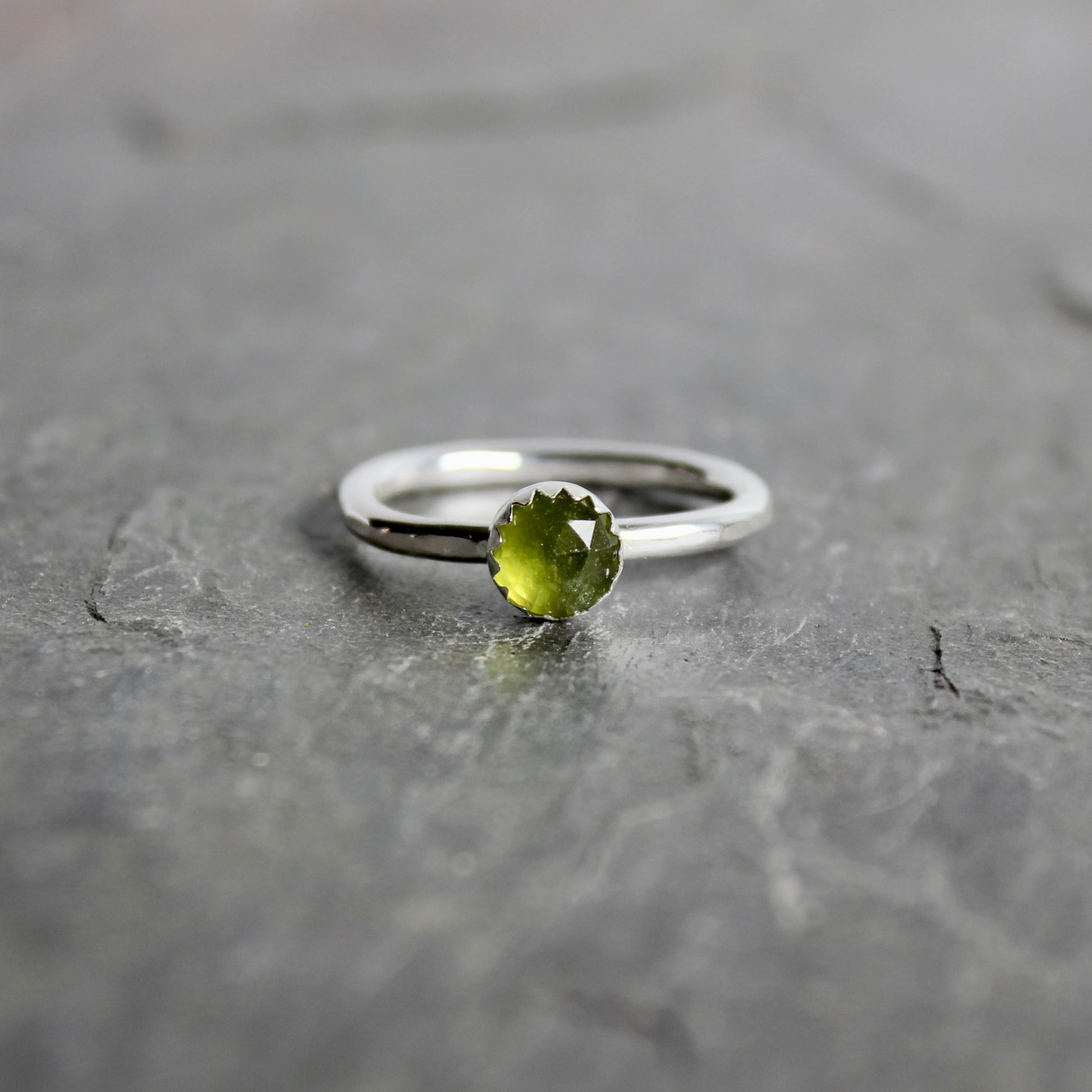 Silver ring with a green serpentine gemstone on a gray surface