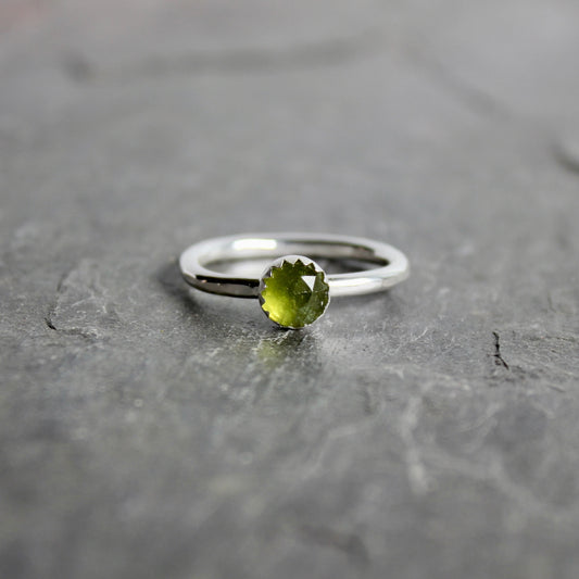 Silver ring with a green serpentine gemstone on a gray surface