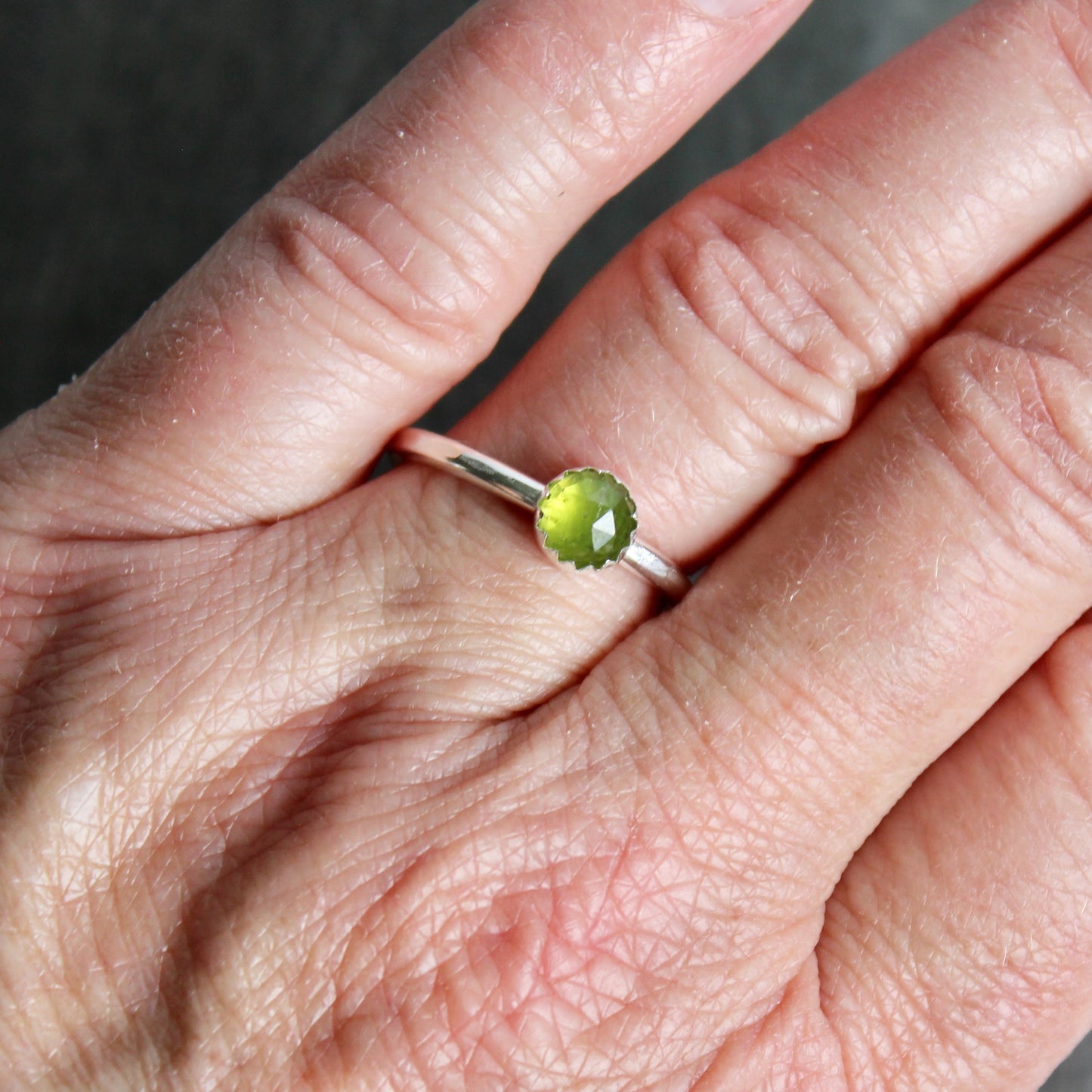 hand with round serpentine gemstone ring on a dark surface