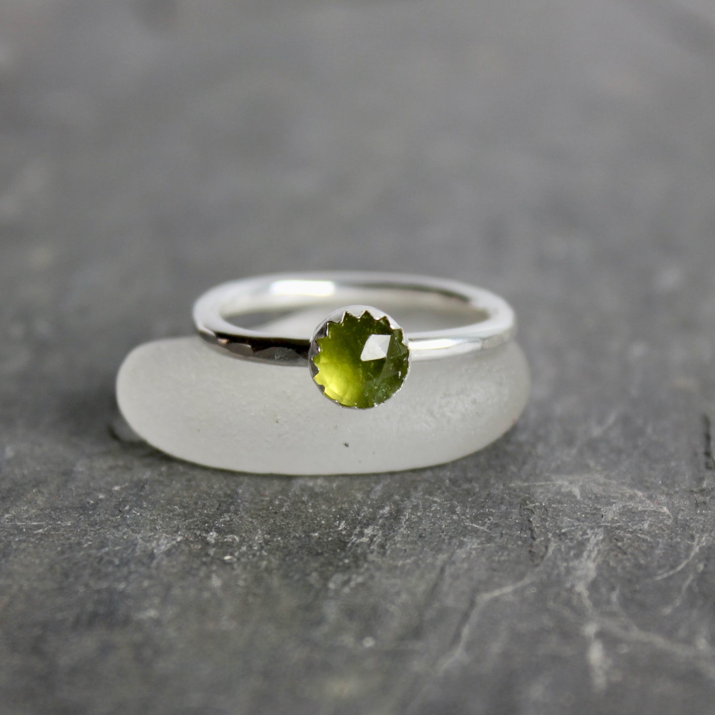 Silver ring with a green serpentine gemstone on a gray surface
