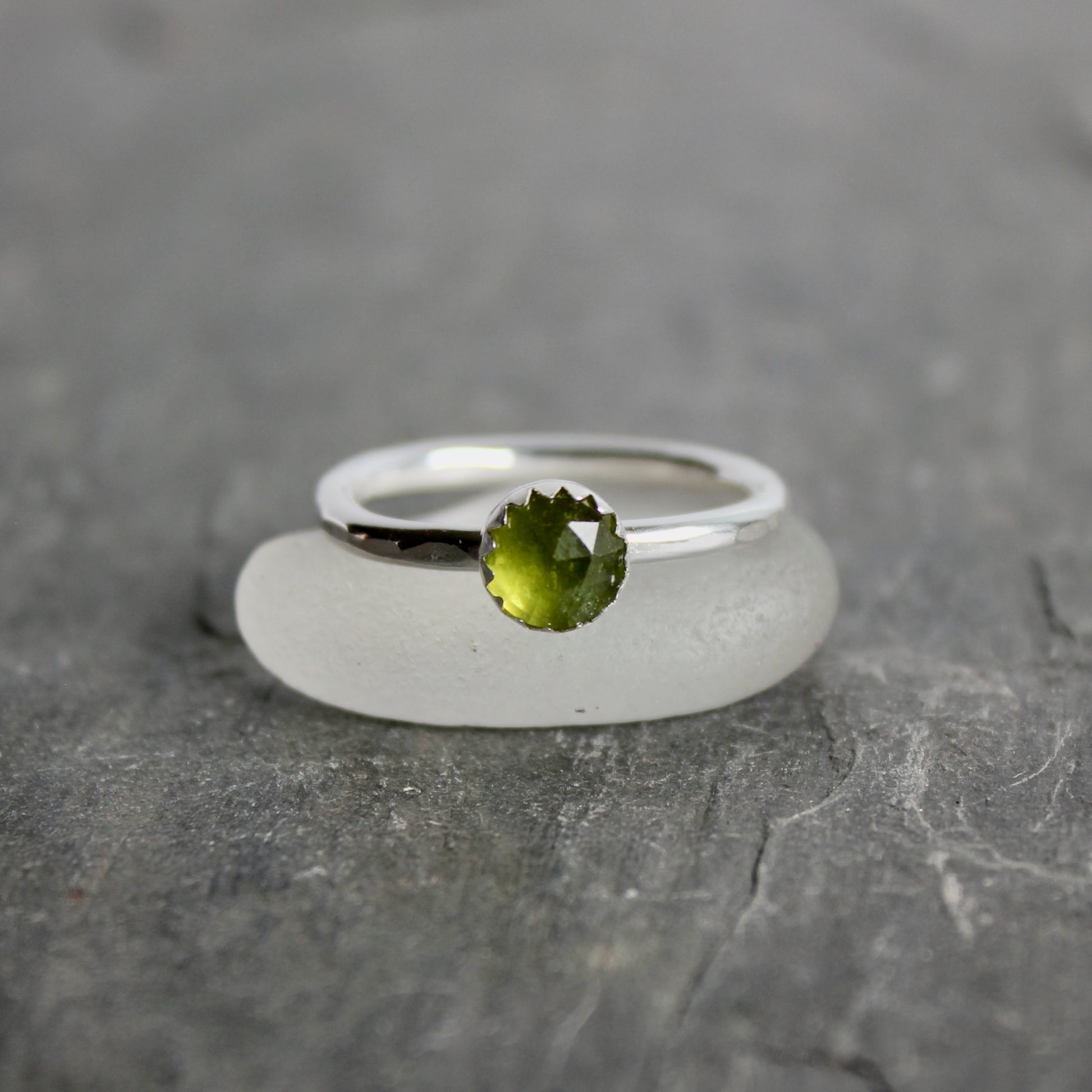 Silver ring with a green serpentine gemstone on a gray surface