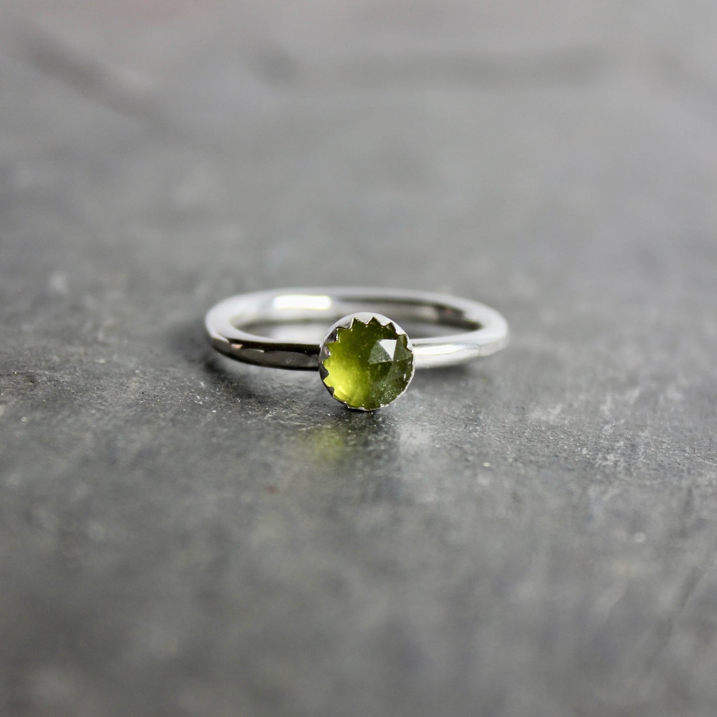 Silver ring with a green serpentine gemstone on a gray surface