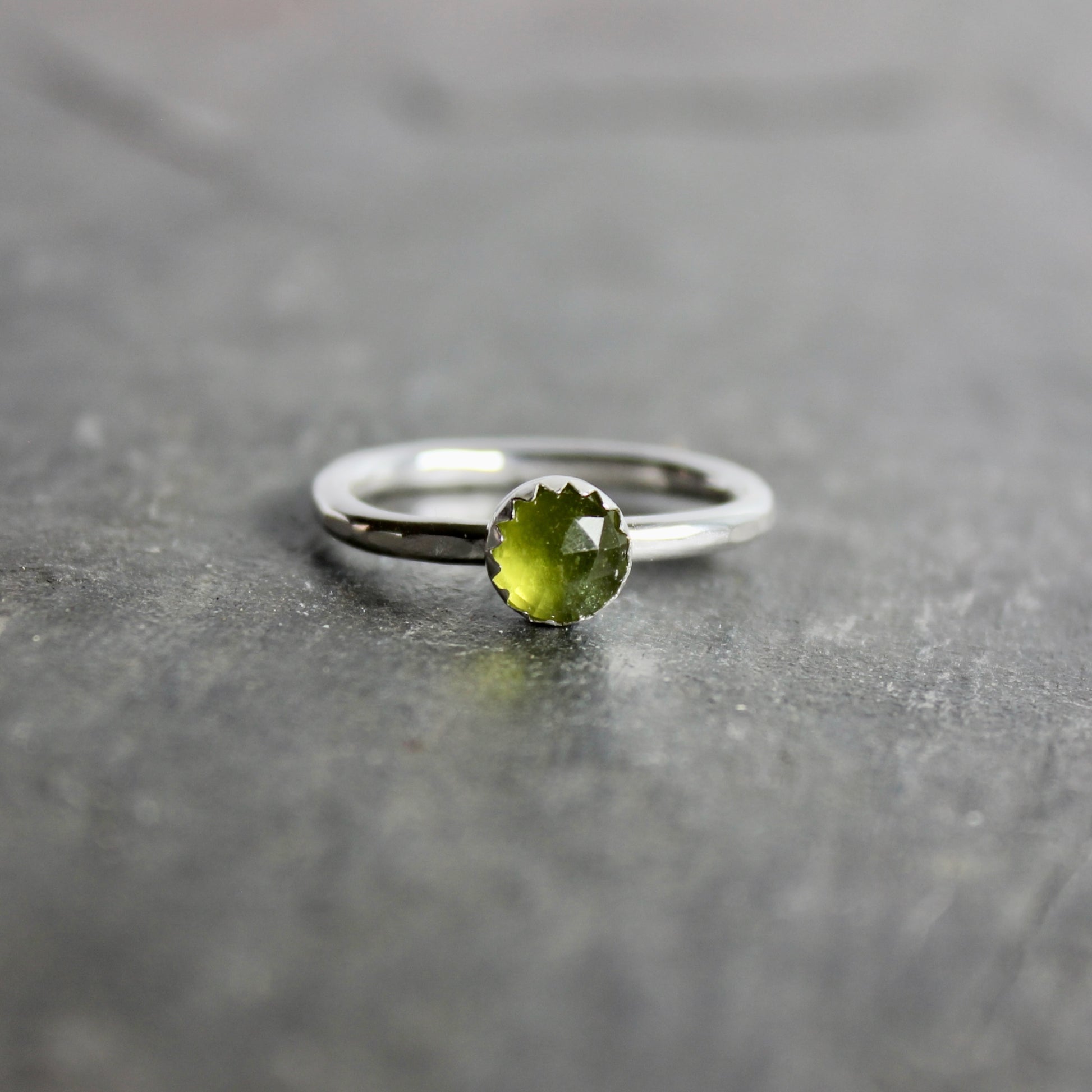 Silver ring with a green serpentine gemstone on a gray surface