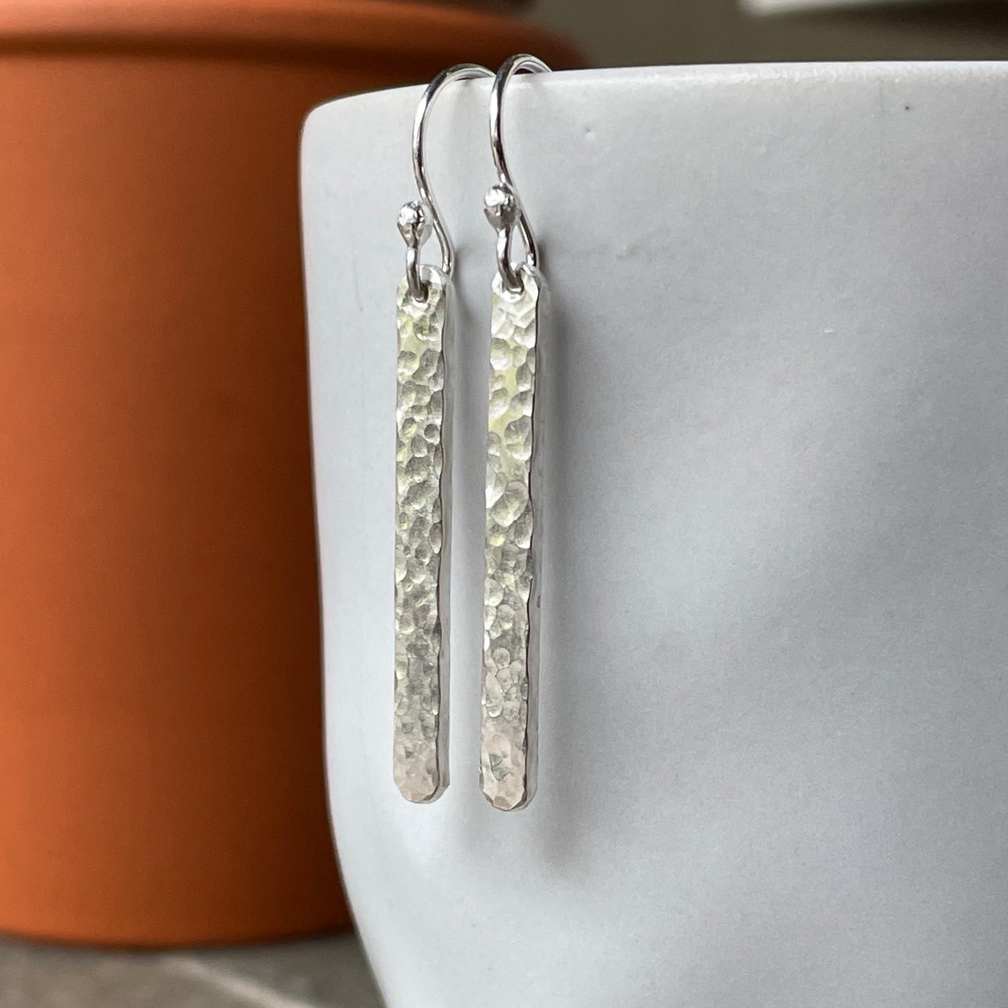Silver bar earrings hanging on a white mug with a terracotta pot in the background.