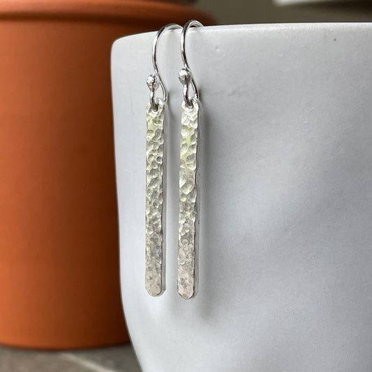 Silver bar earrings hanging on a white mug with a terracotta pot in the background.