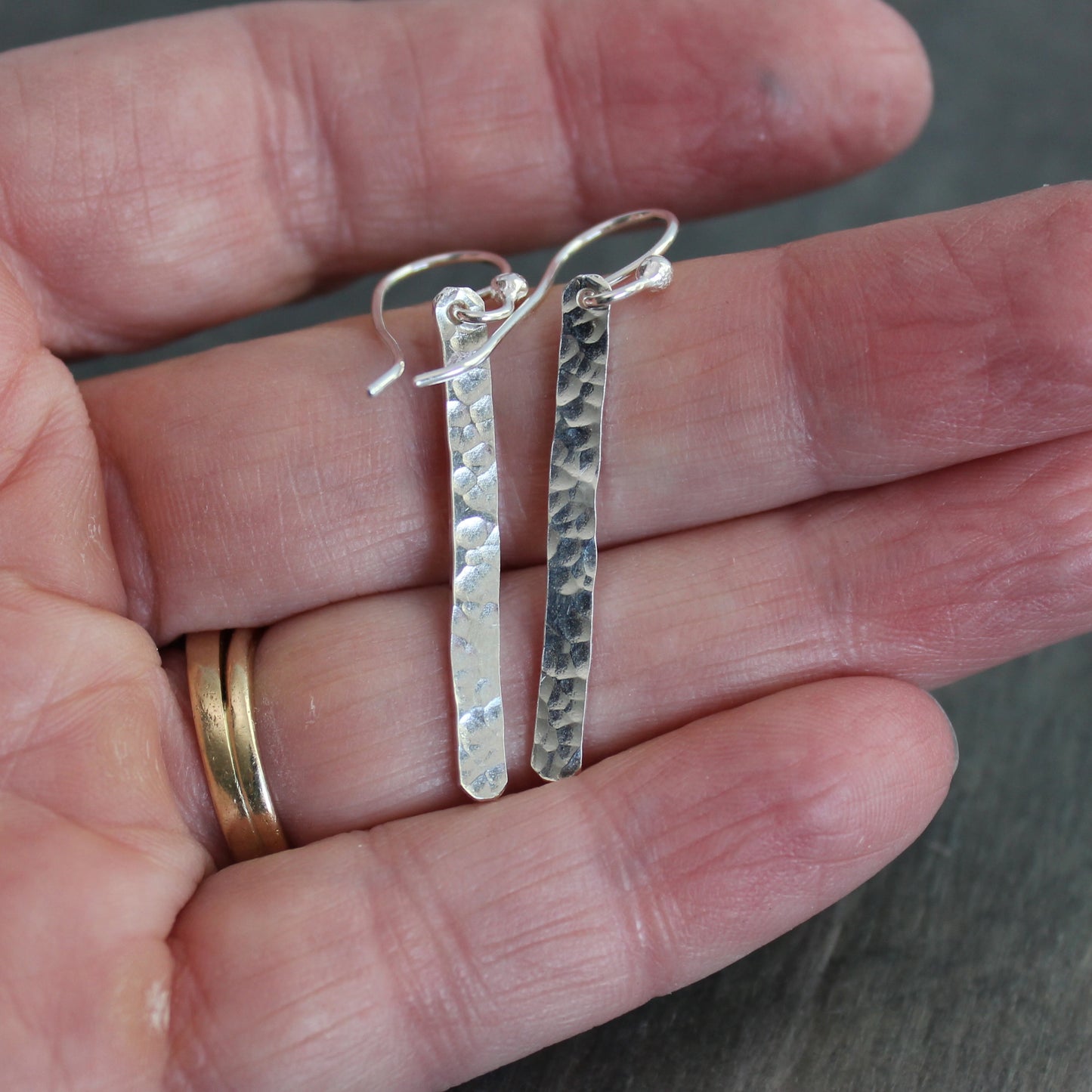 Silver earrings held between fingers with a blurred background