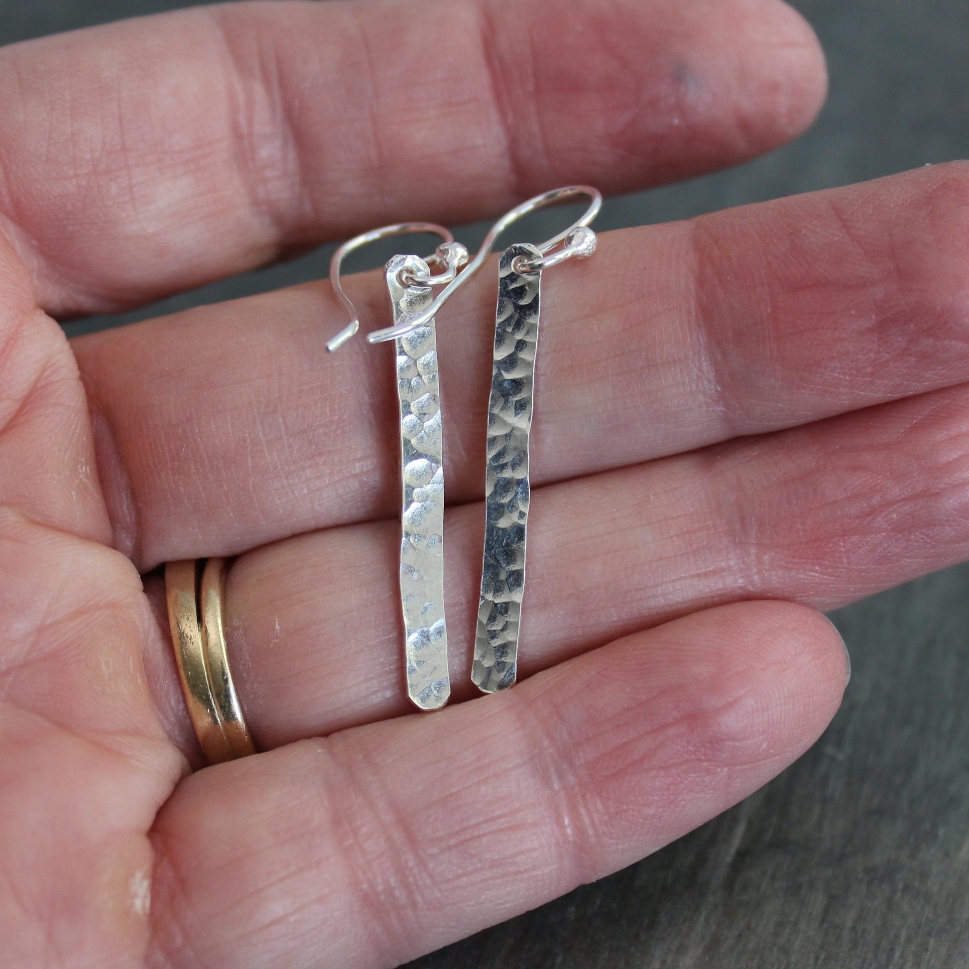 Silver earrings held between fingers with a blurred background
