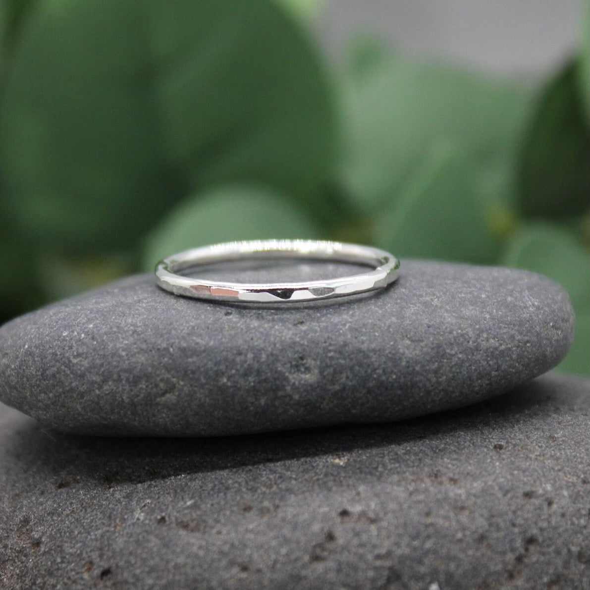 Silver ring on a gray stone with green foliage in the background