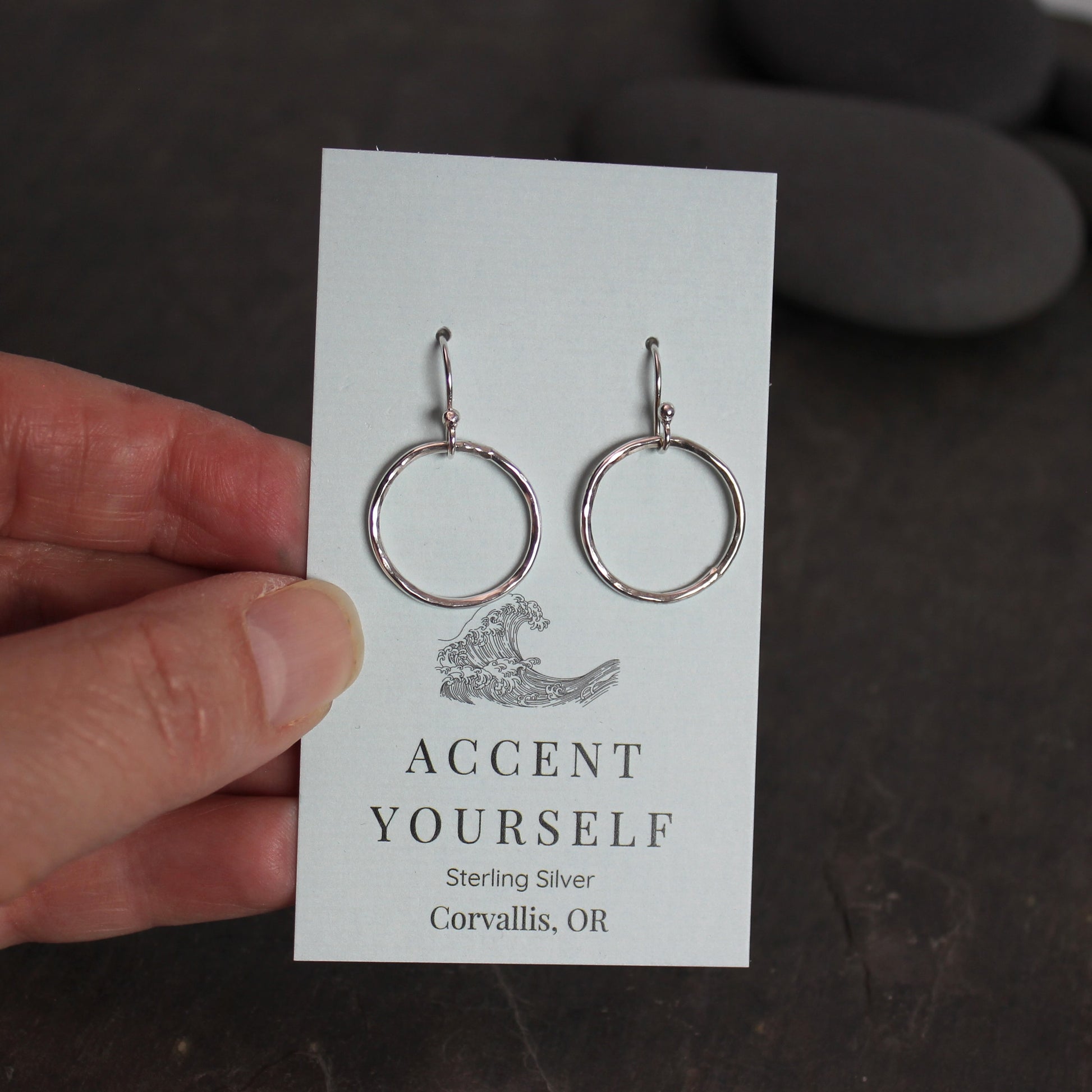 Silver hoop earrings on a card held by a hand with a blurred background