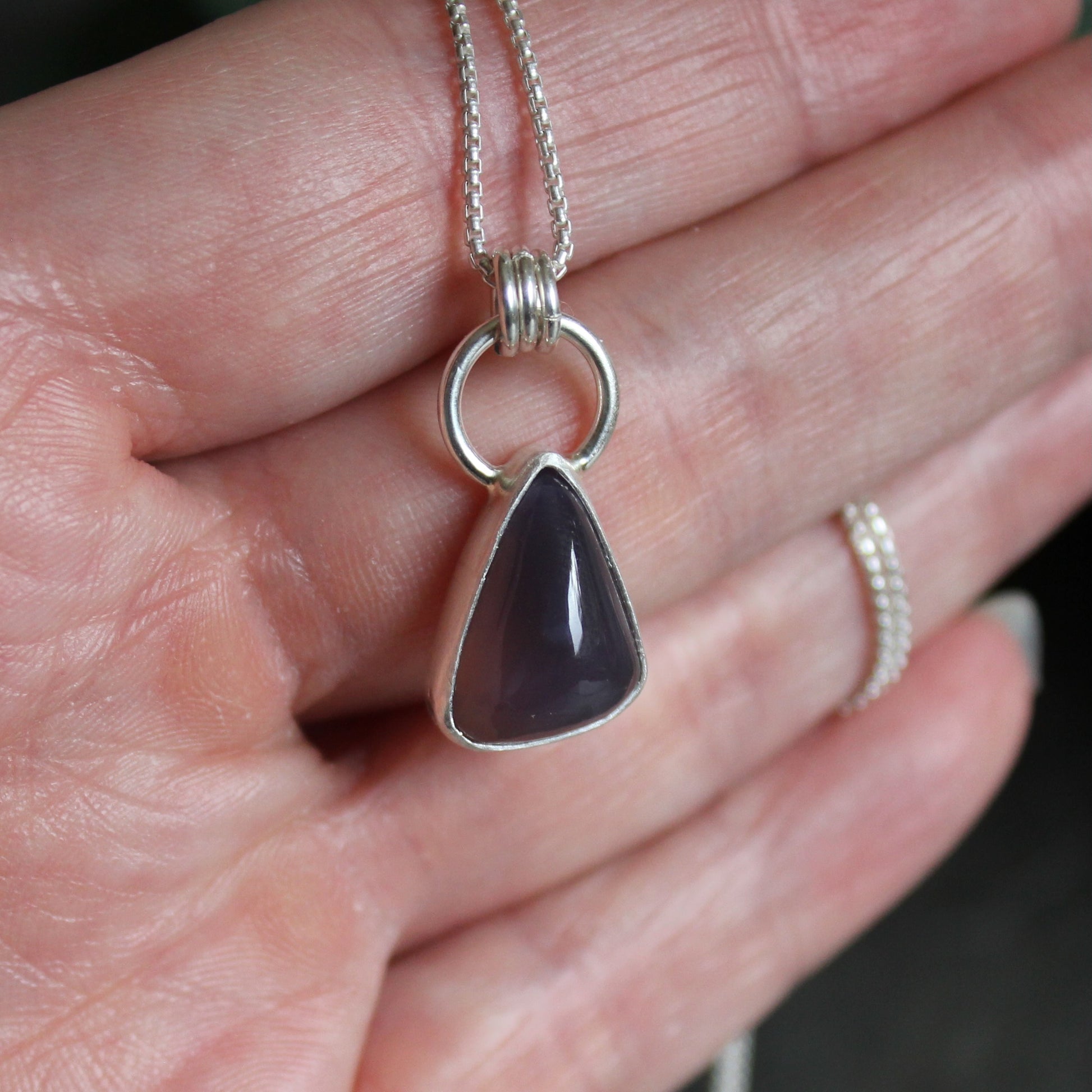 This is a small dark Holley blue agate set in a fine & sterling silver bezel setting and comes with an 18" chain. This stone is triangular shaped