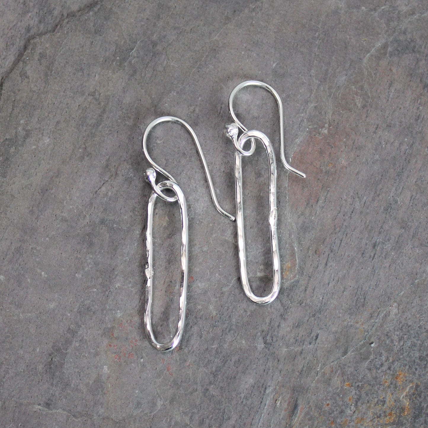 Pair of silver earrings on a gray stone surface