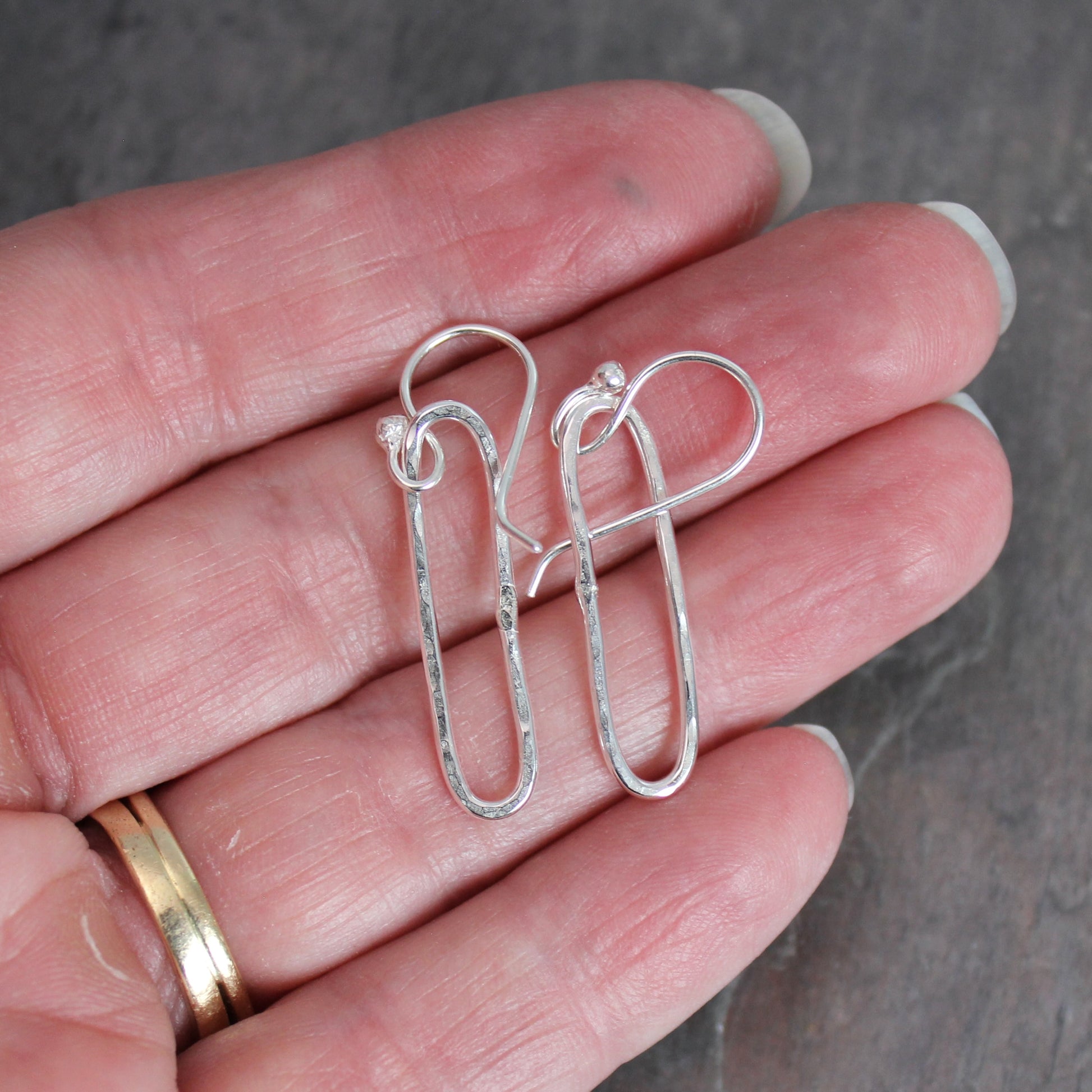 Silver earrings held in a hand against a neutral background