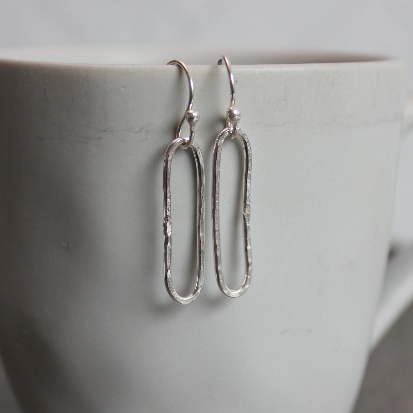 Silver earrings hanging on a white mug