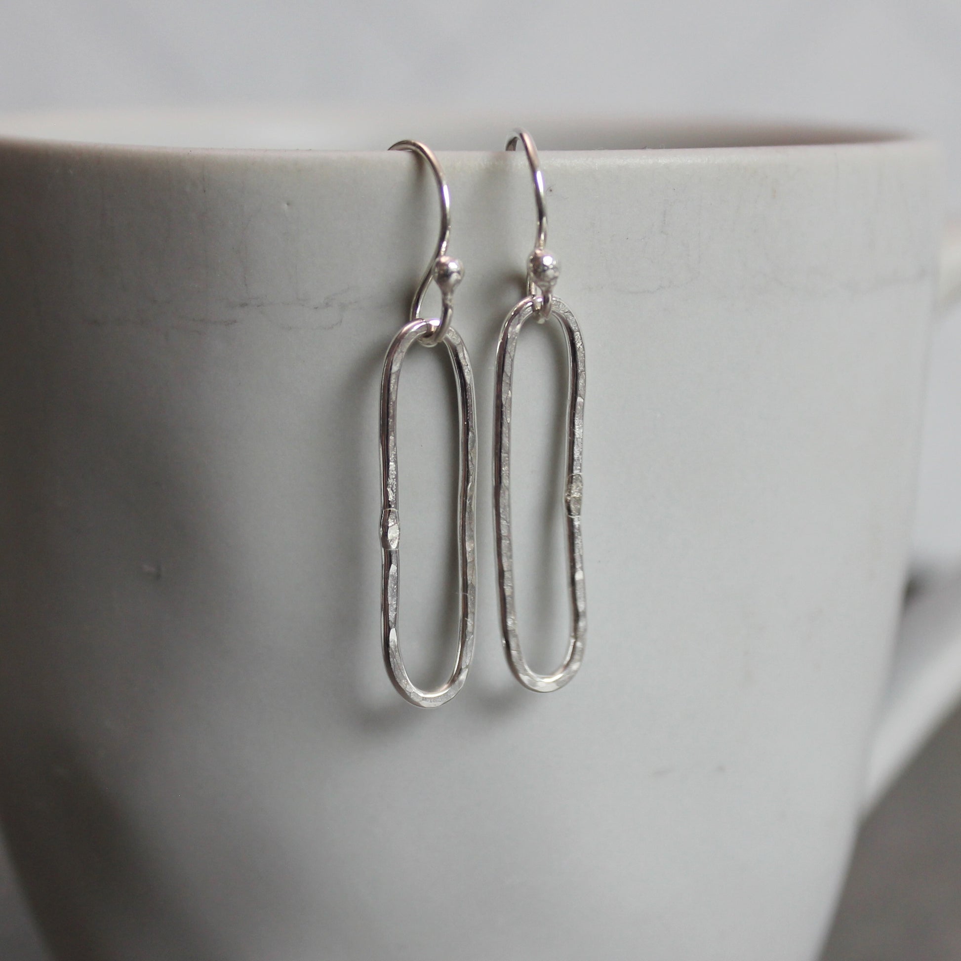 Silver earrings hanging on a white mug