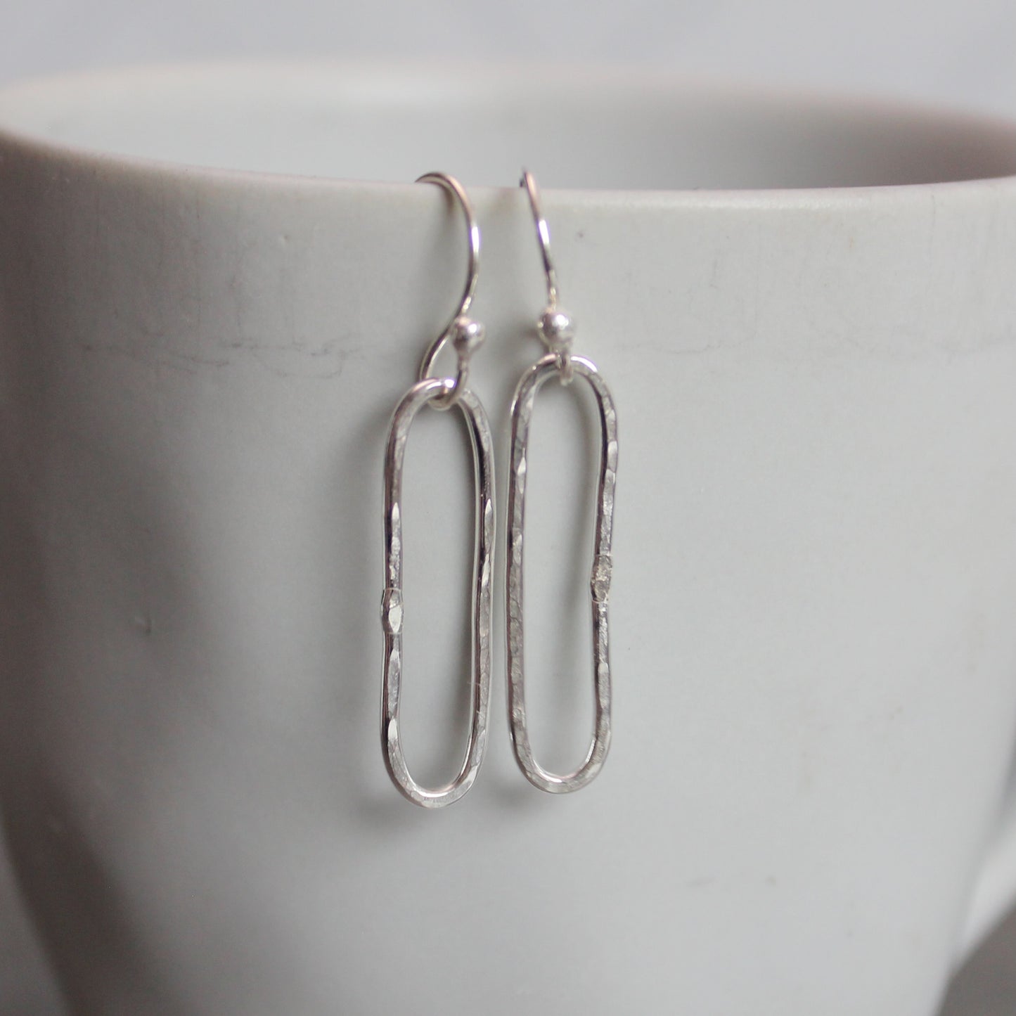 Silver earrings on a white ceramic cup
