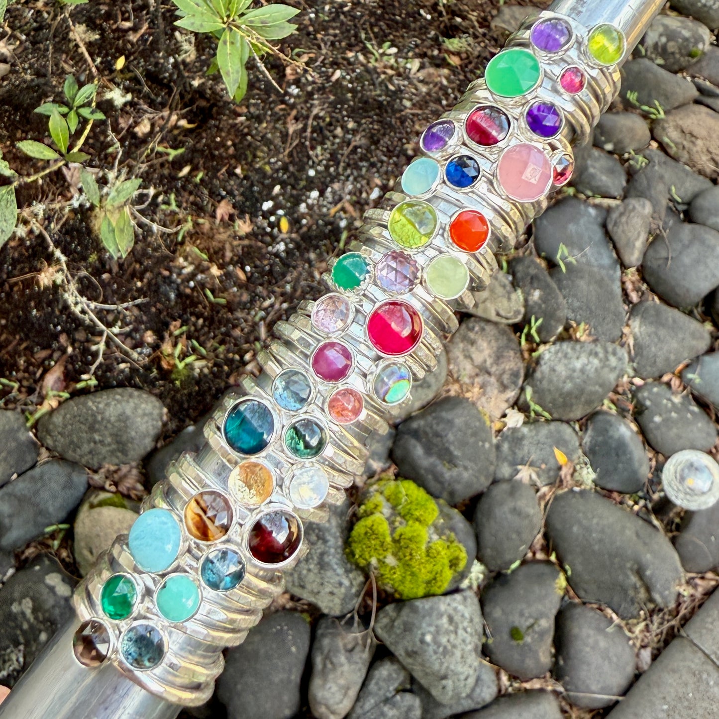 Decorative garden hose with colorful gemstones on a stone and soil background