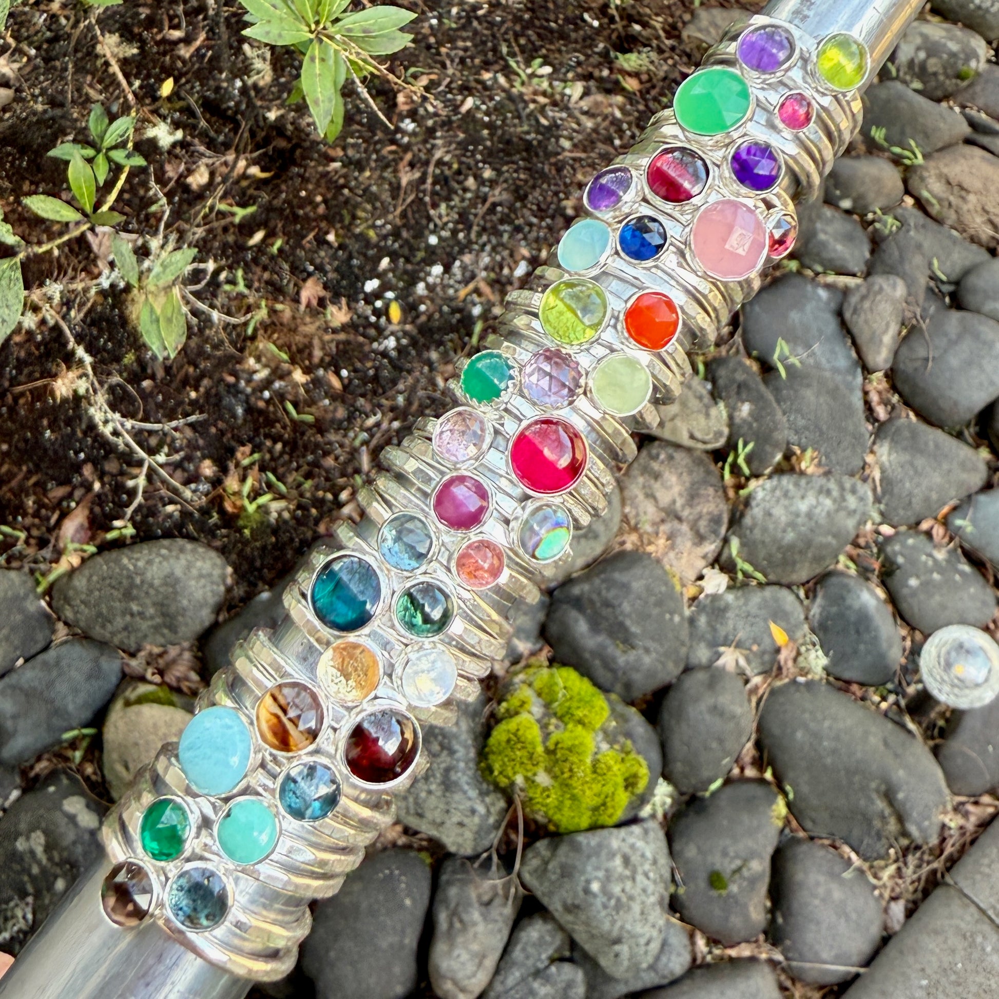 Decorative garden hose with colorful gemstones on a stone and soil background