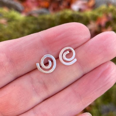 Handmade sterling silver spiral studs held between two fingers.