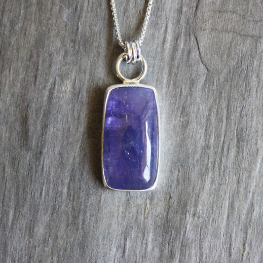 Tanzanite pendant on a silver chain against a wooden background