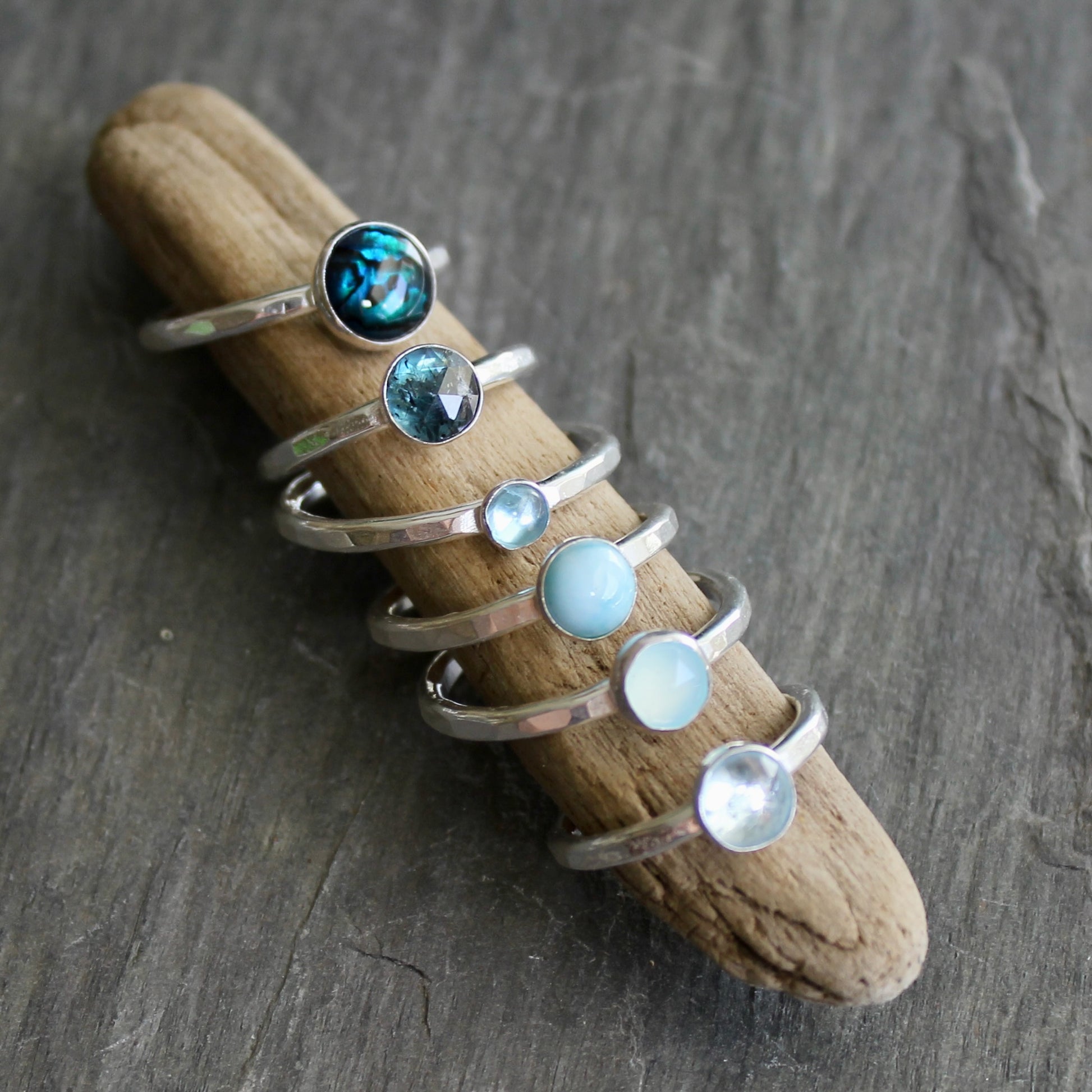 Set of silver rings with gemstones on a piece of driftwood against a gray stone background