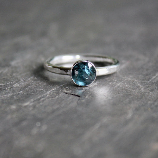 Silver ring with a teal kyanite gemstone on a gray surface
