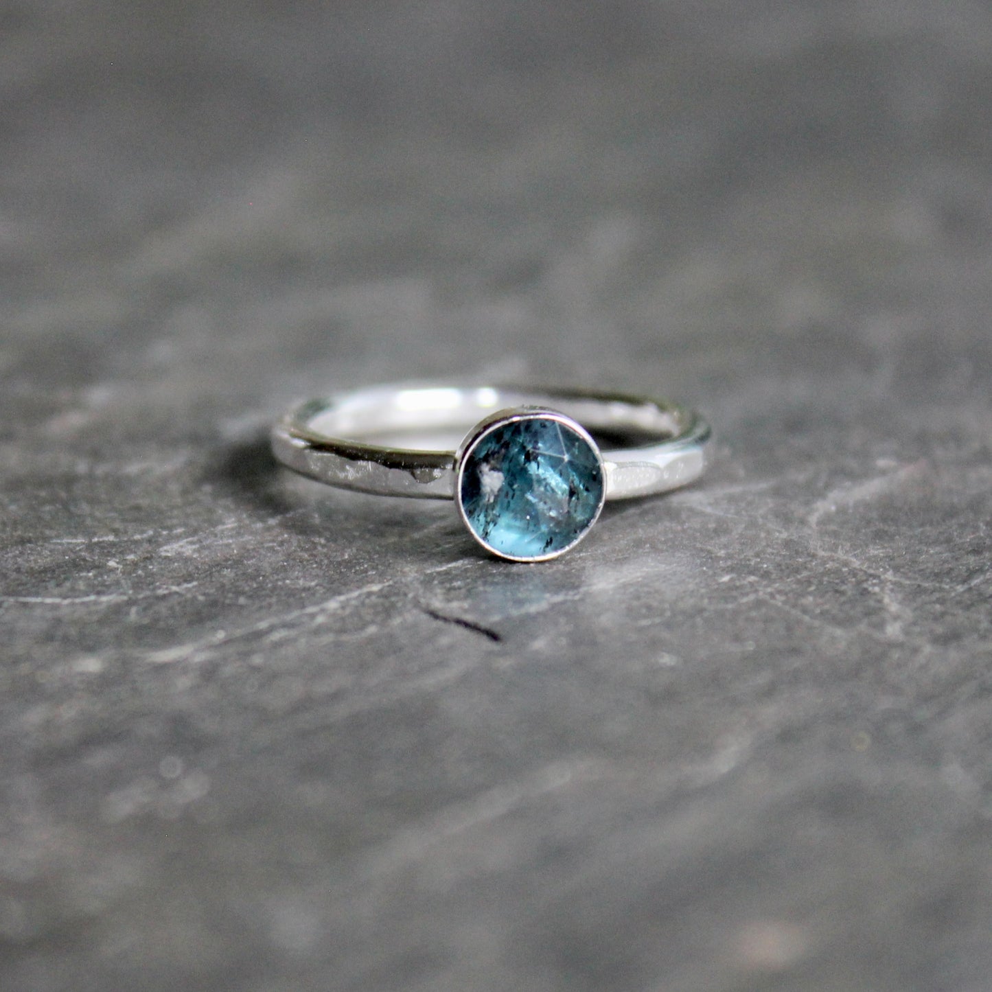 Silver ring with a teal kyanite gemstone on a gray surface