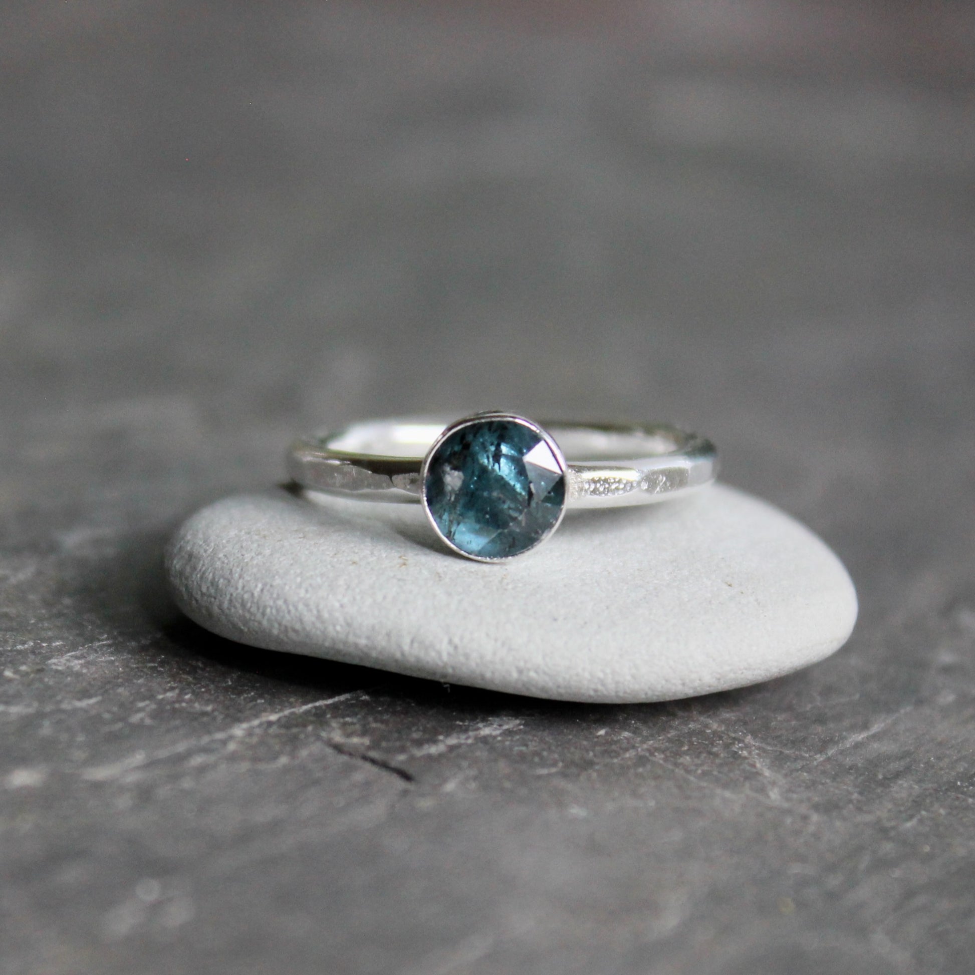 Silver ring with a teal kyanite gemstone on a gray surface