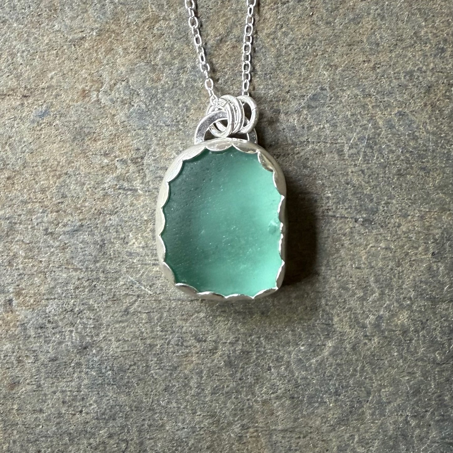 Teal sea glass pendant necklace on a stone surface