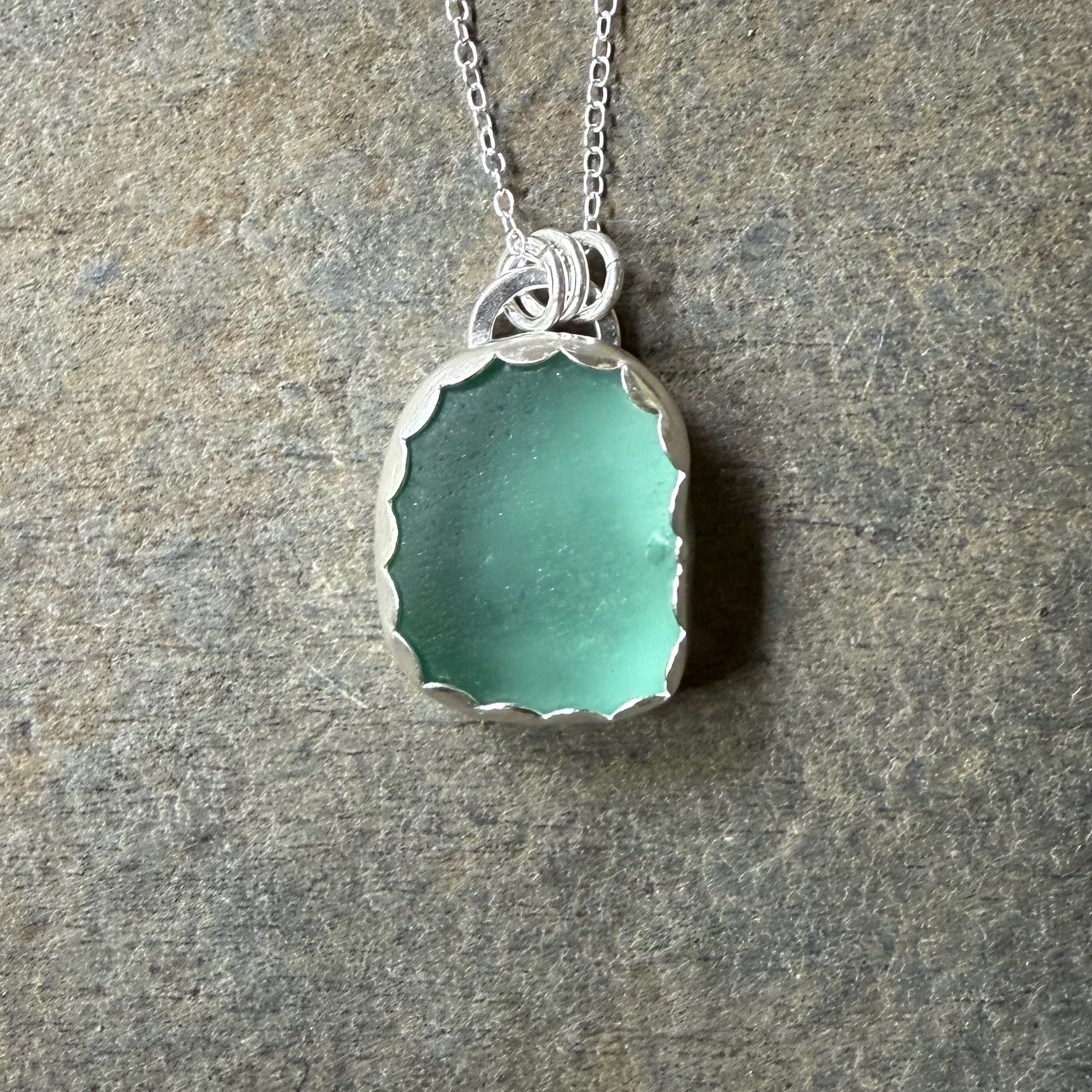 Teal sea glass pendant necklace on a stone surface