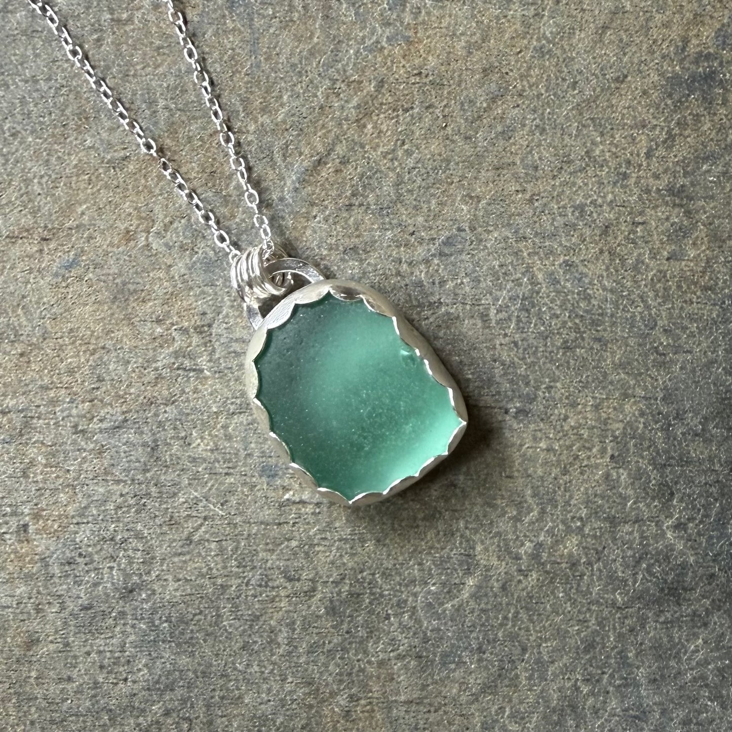 Necklace with a green sea glass pendant on a stone surface