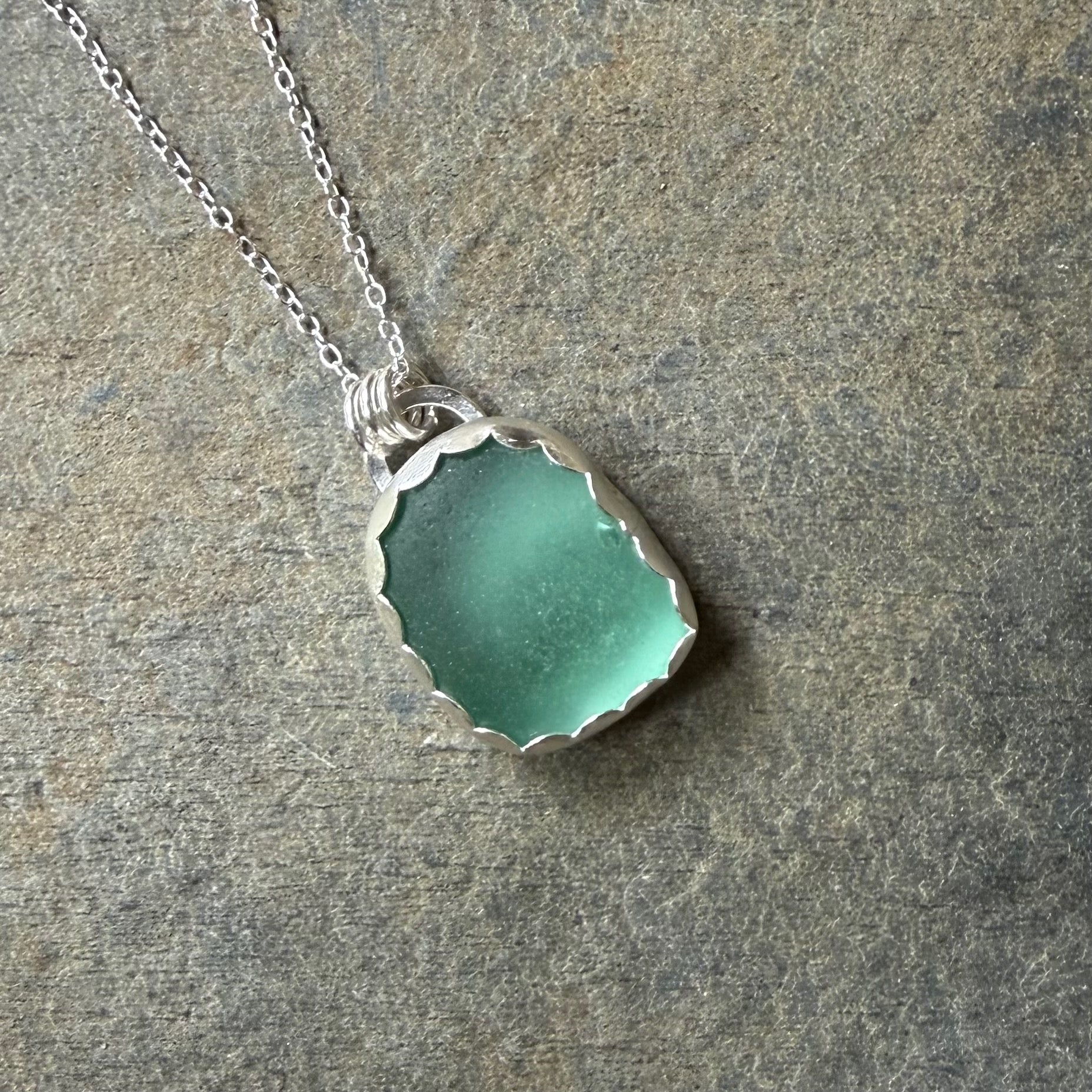 Necklace with a green sea glass pendant on a stone surface