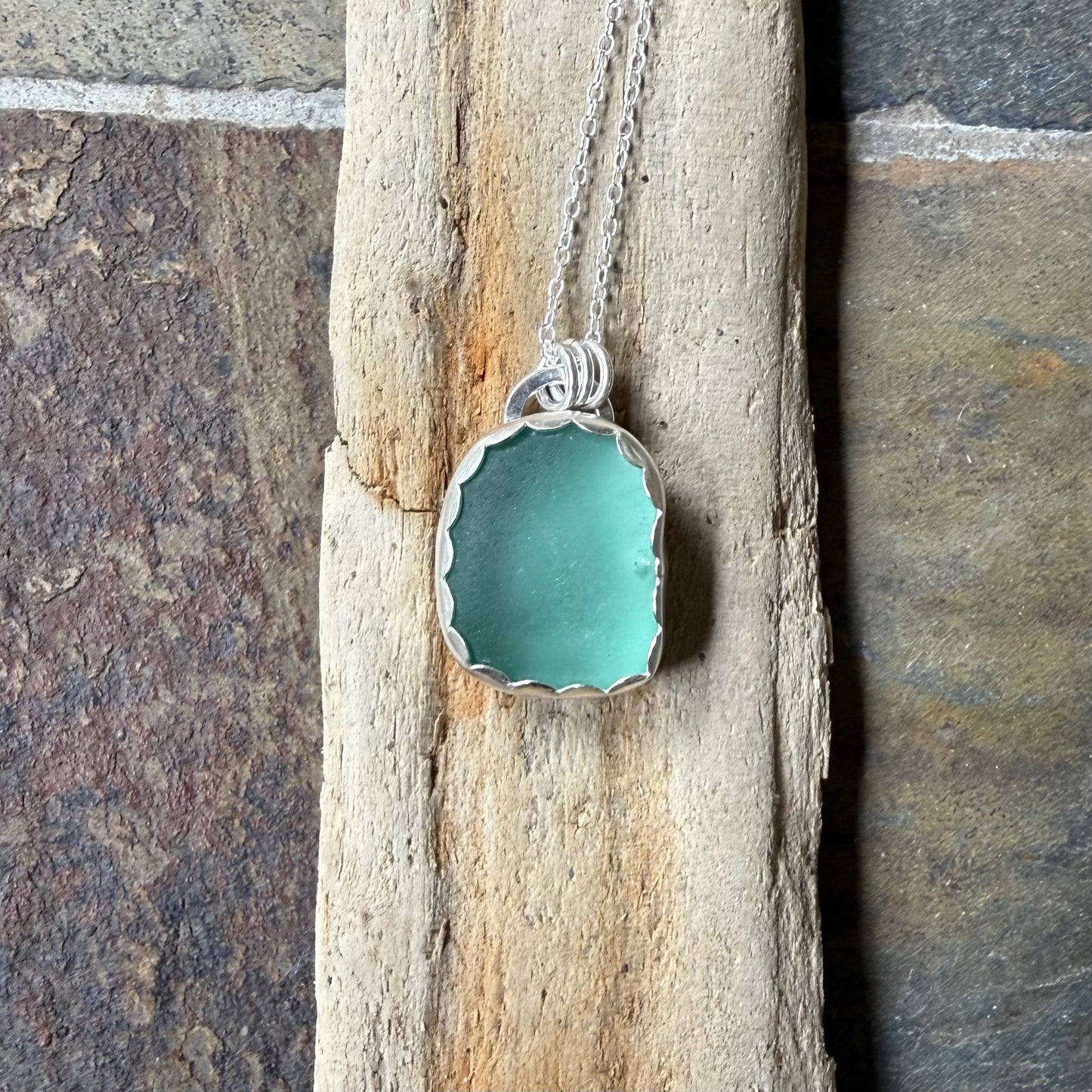 Turquoise sea glass pendant necklace on a wooden stick with a stone background