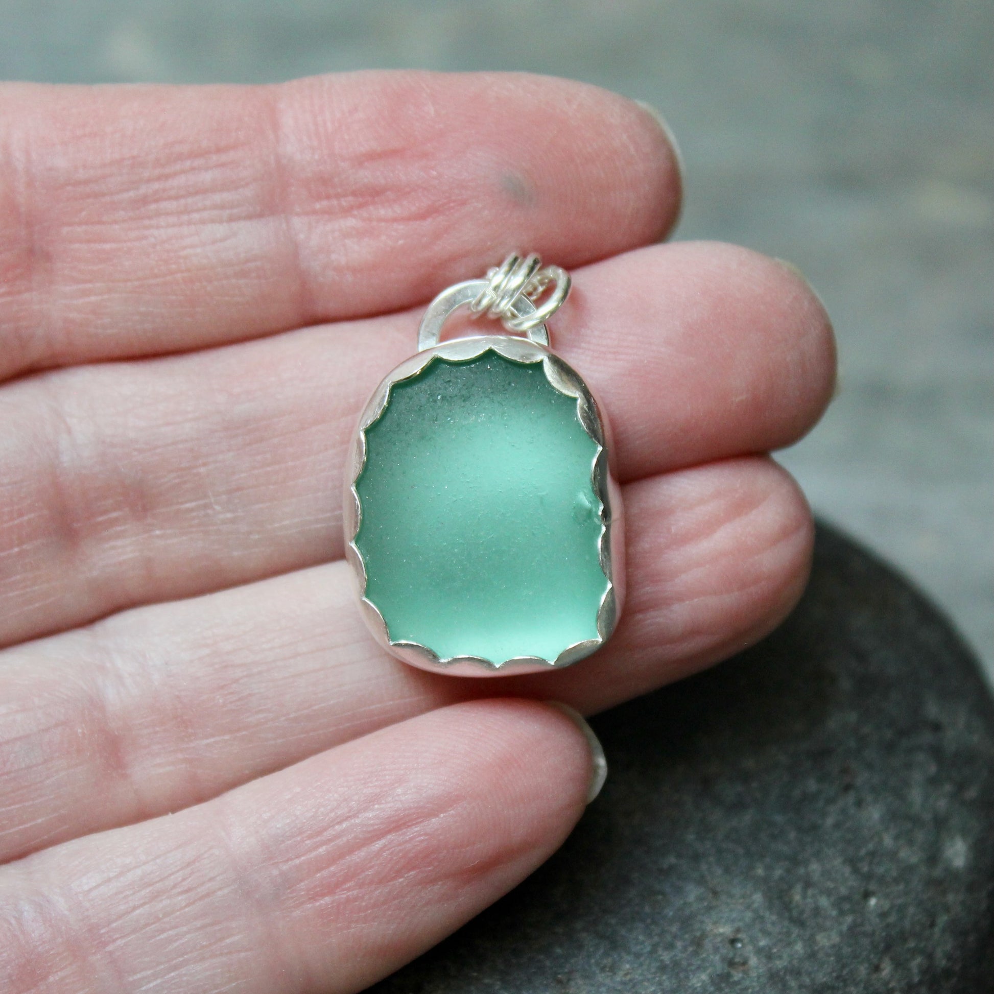 Teal Sea Glass pendant held in a hand with a blurred background