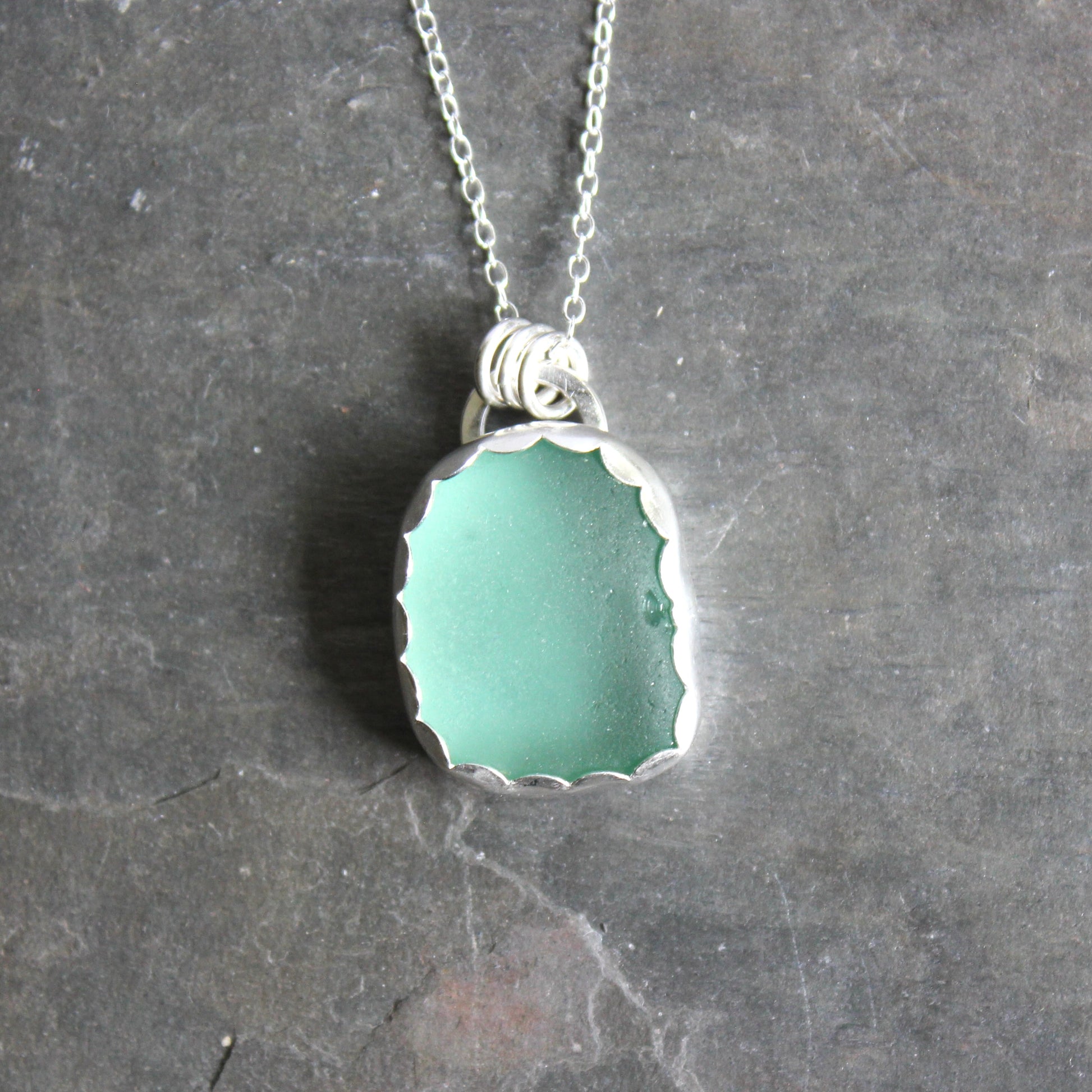 Teal sea glass pendant necklace on a dark gray background