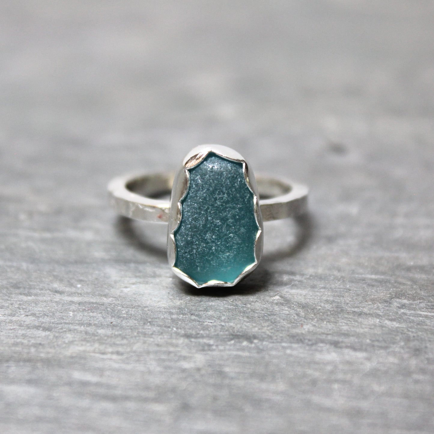 Dark turquoise sea glass ring with silver band on a gray surface