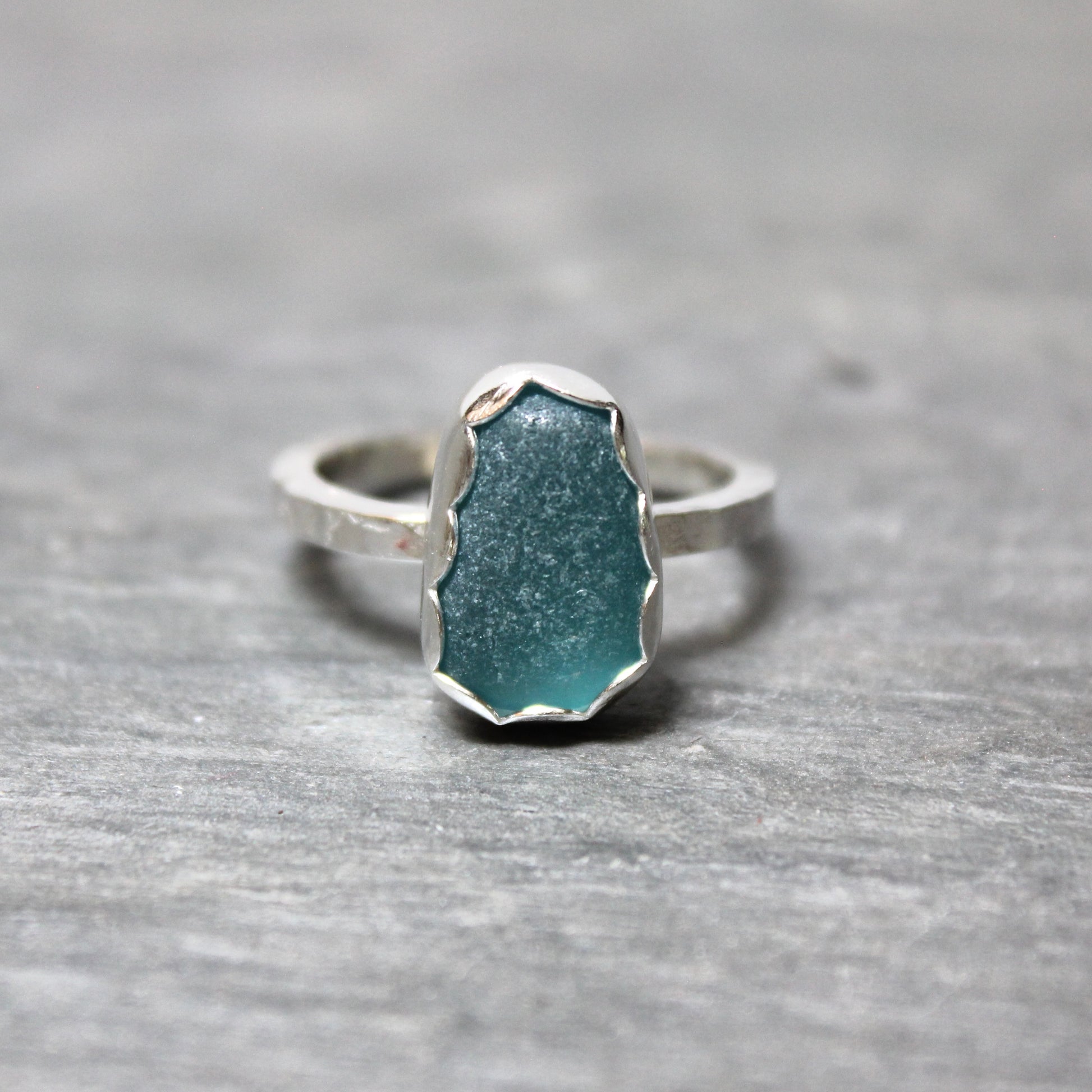 Dark turquoise sea glass ring with silver band on a gray surface