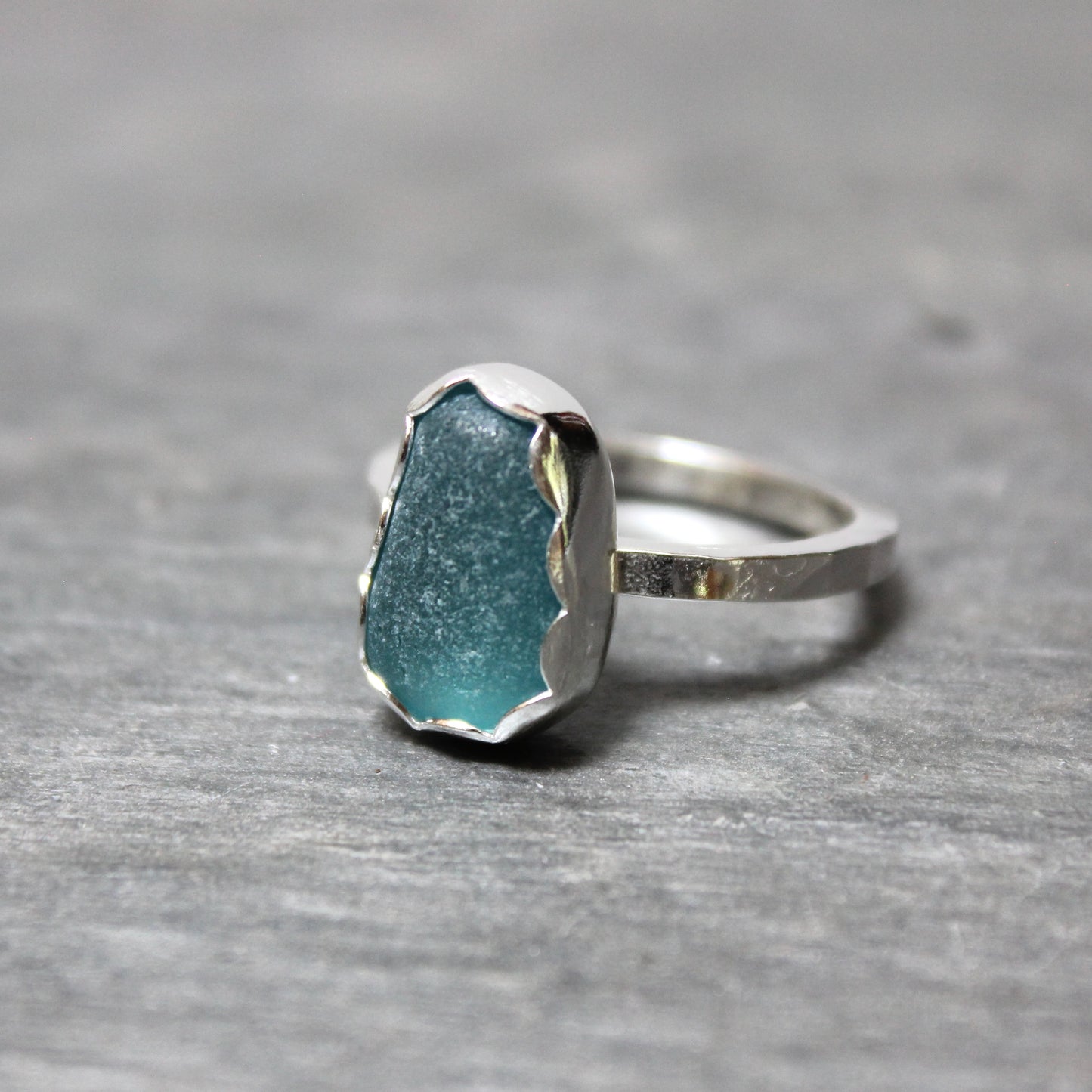 Dark turquoise sea glass ring with silver band on a gray surface