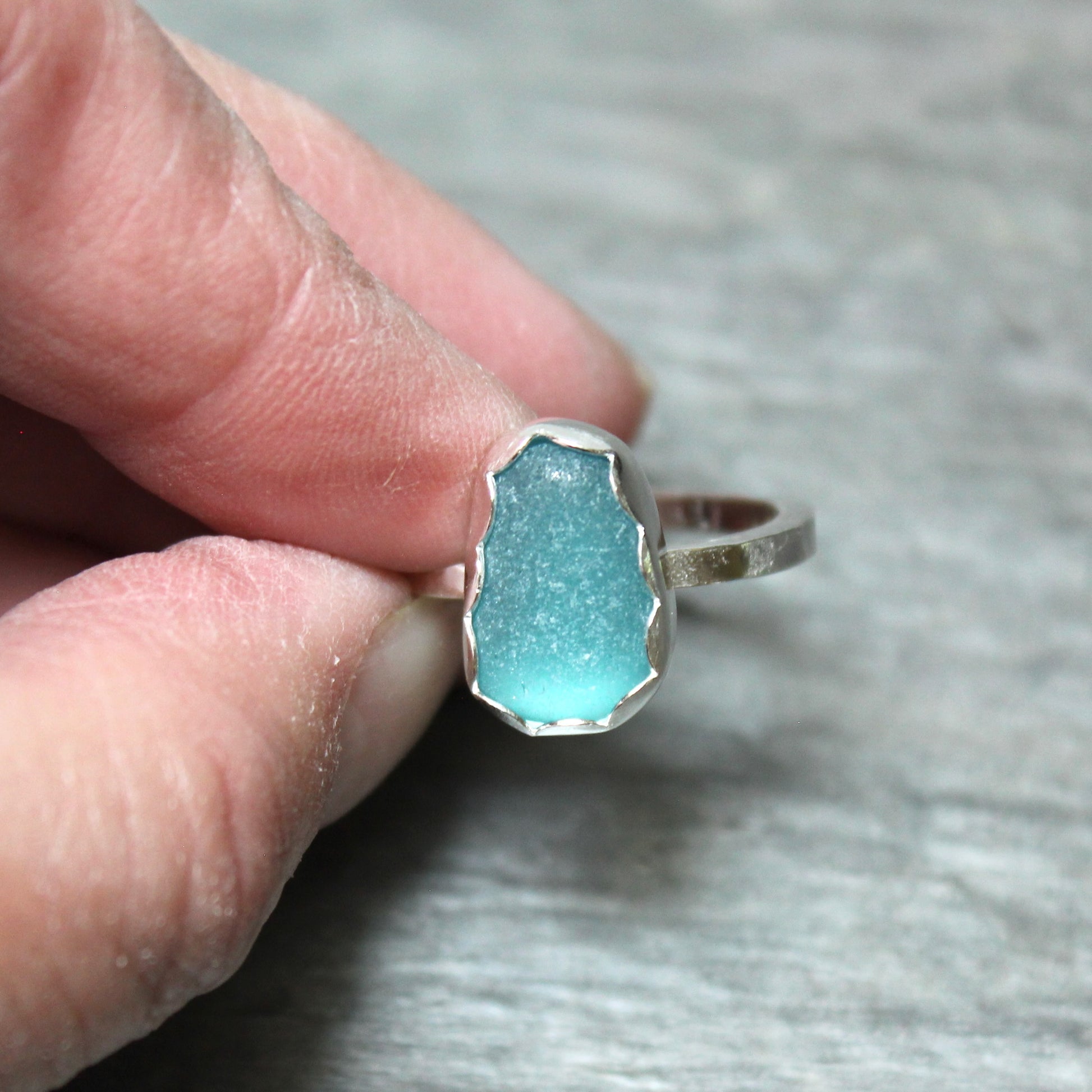 Turquoise sea glass ring with silver band held between fingers on a neutral background