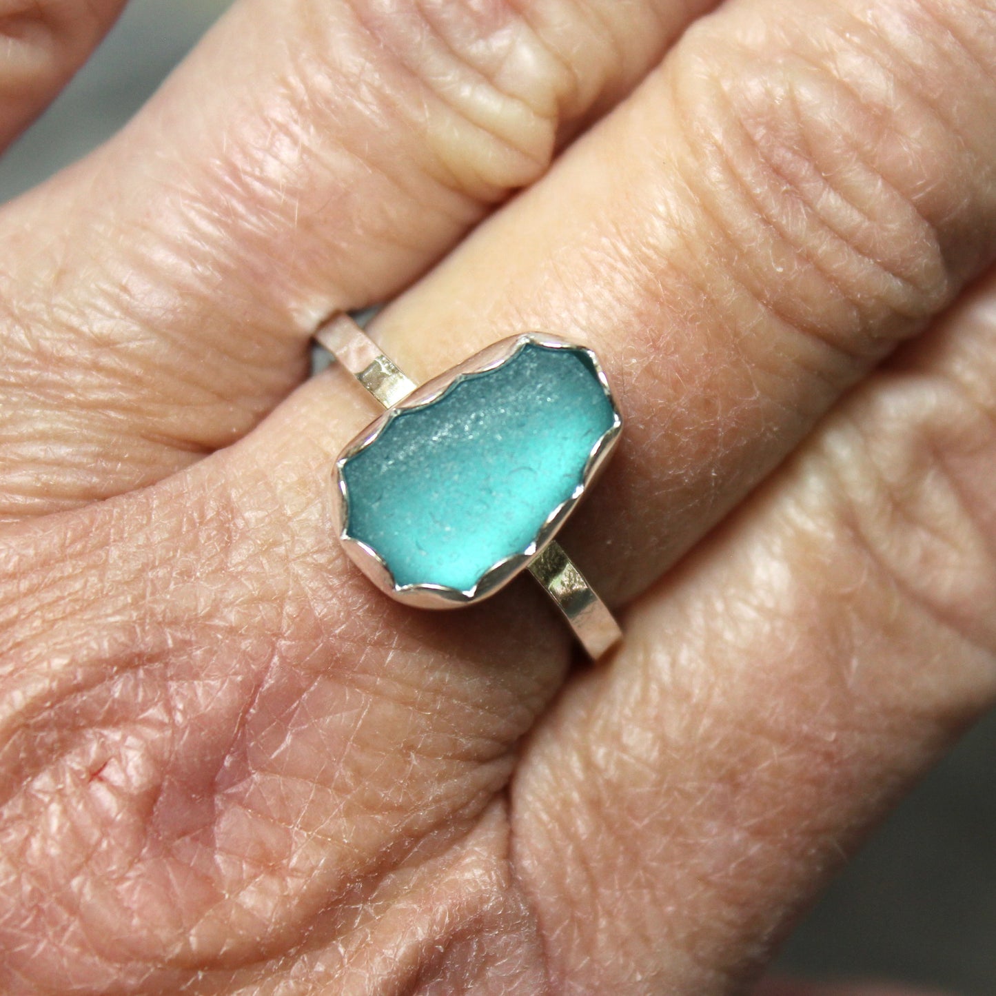 Dark turquoise sea glass ring on a person's finger