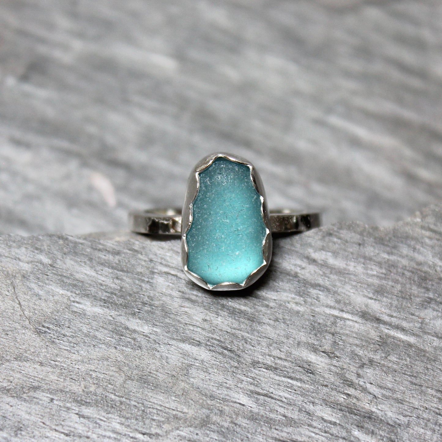 Dark turquoise sea glass ring with silver band on a gray surface